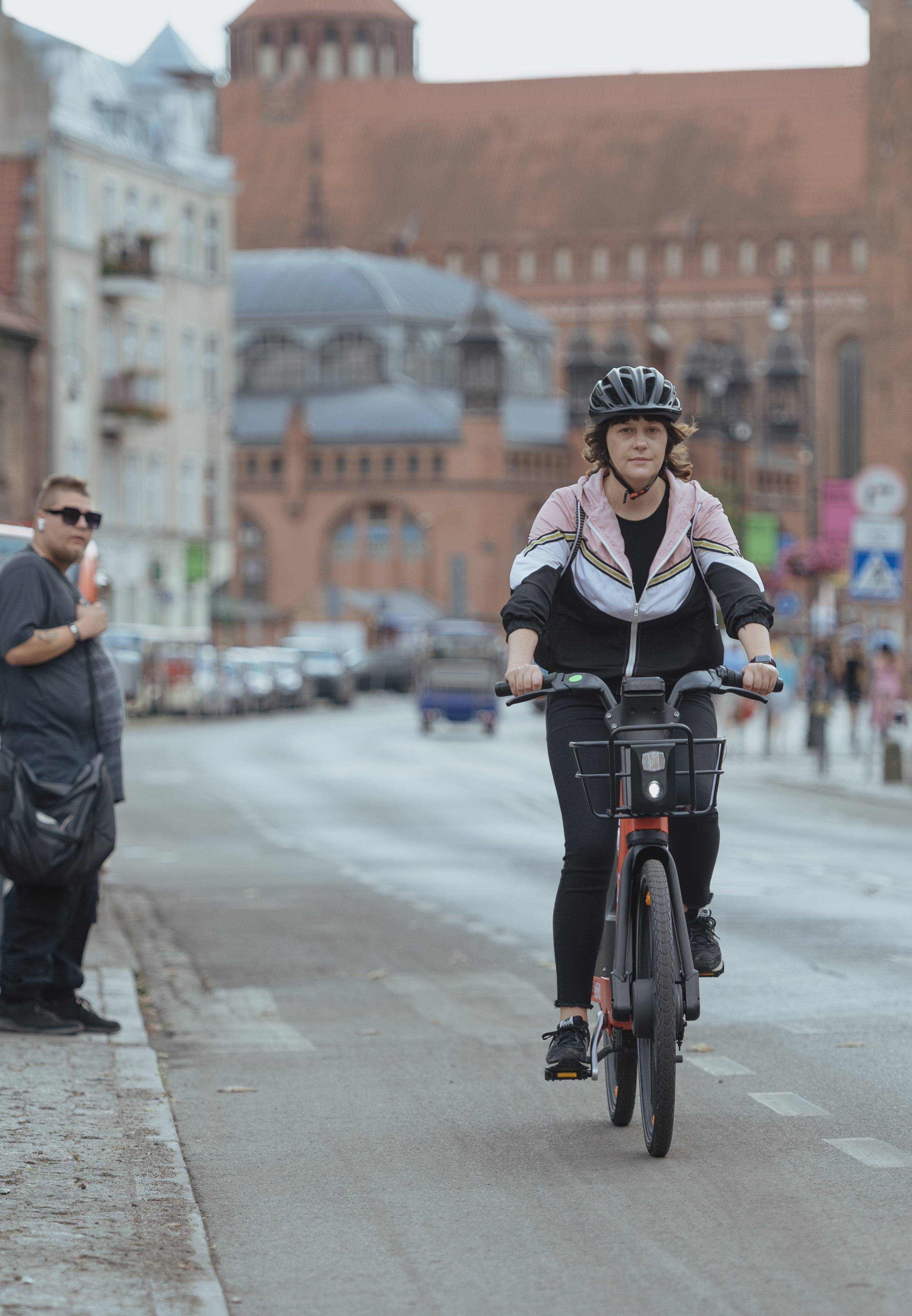 kobieta jadąca przez centrum gdańska rowerem elektrycznym, w tle kamienice i hala targowa
