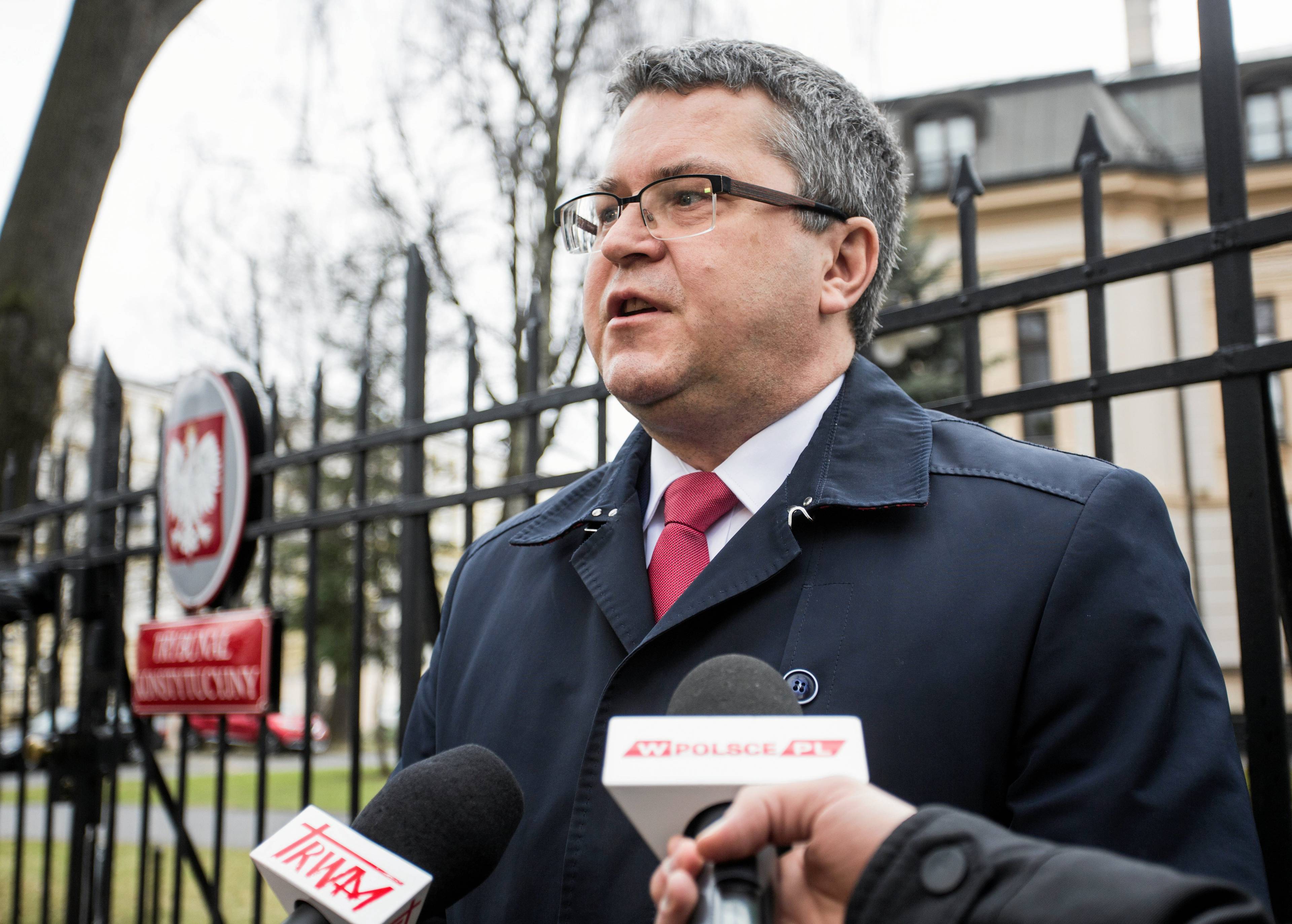 Mężczyzna w okularach stoi na tle metalowego płotu Trybunału Konstytucyjnego. Jarosław Dudzicz