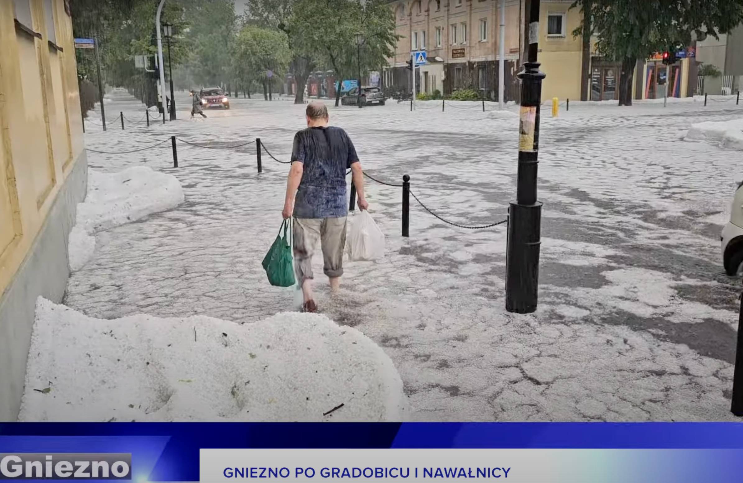 Mężczyzna brnie przez ulicę zalaną deszczem i gradem. Fragment nagrania od TV Gniezno.