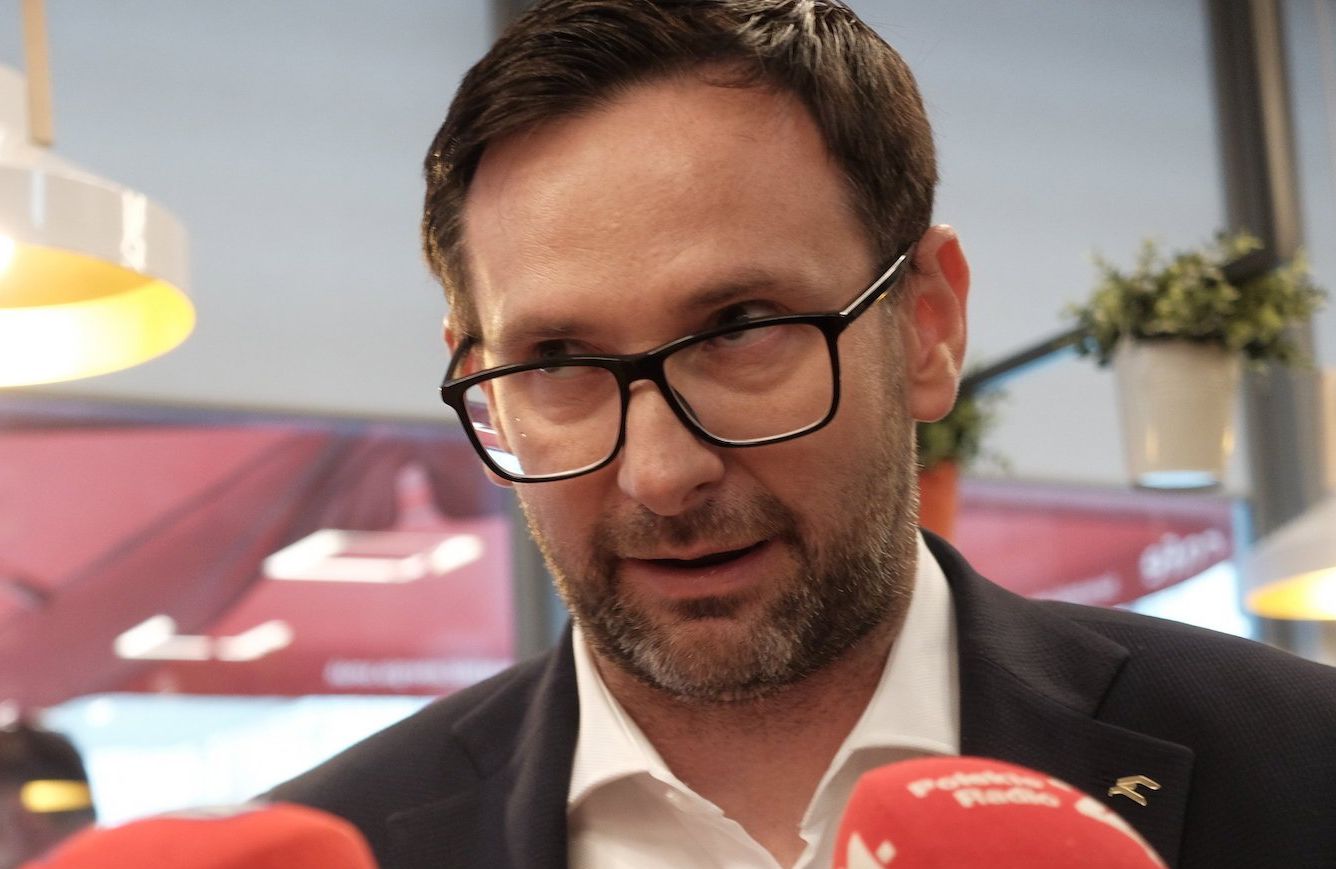 Daniel Obajtek odpowiada na pytania dziennikarzy. Ma ciemną marynarkę i rozpiętą pod szyją białą koszulę.