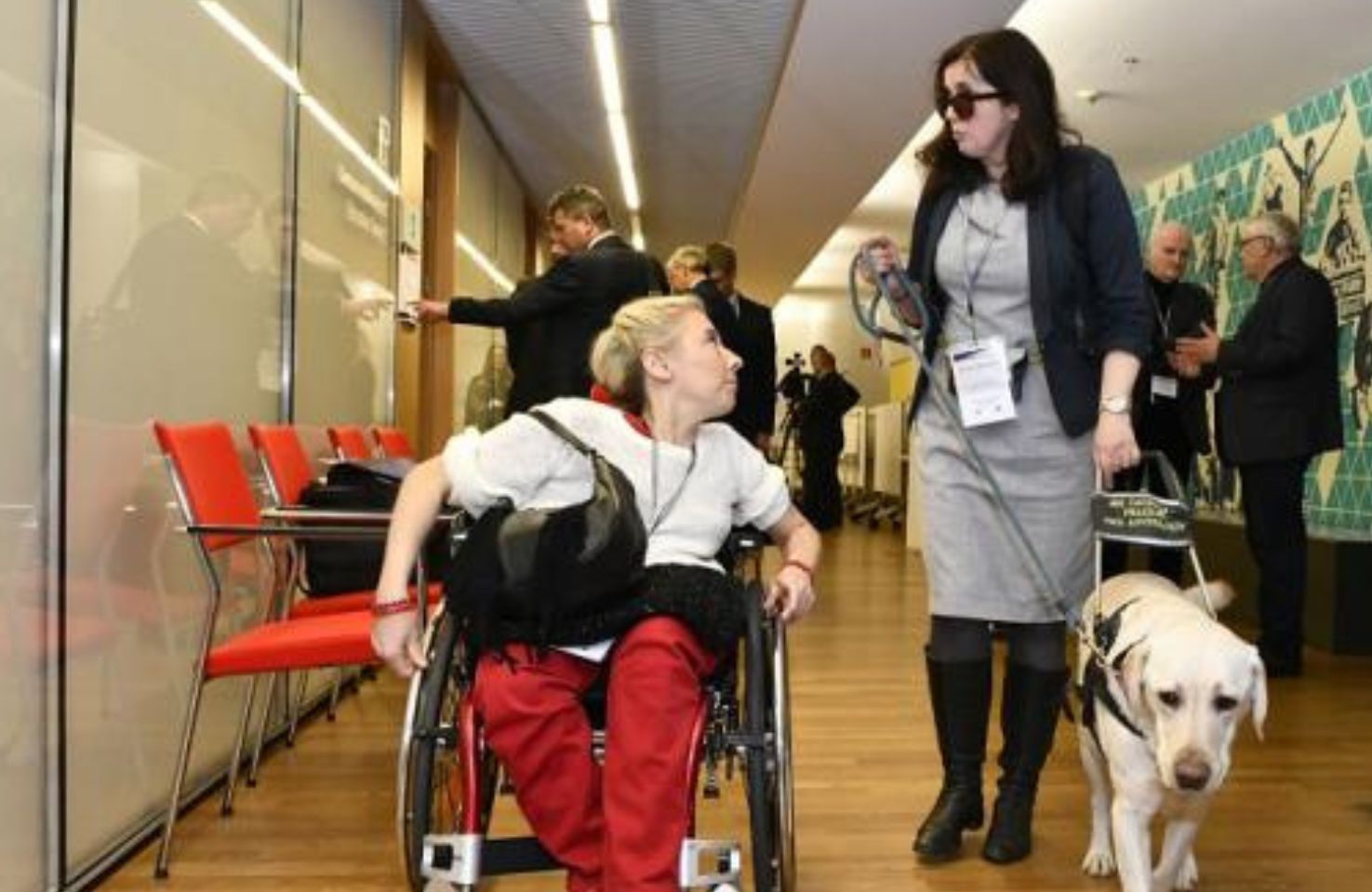 Kobieta na wózku i kobieta z psem asystującym (Jolanta Kramarz)rozmawiają w kuluarach