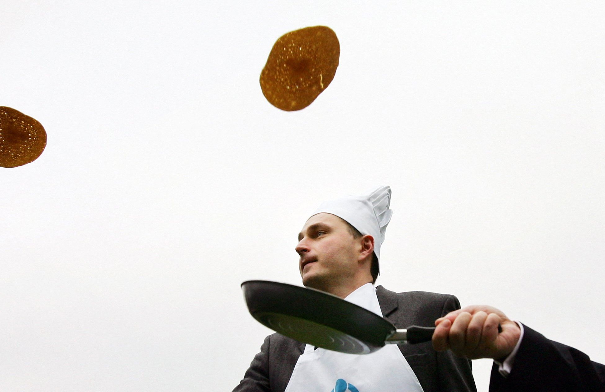 mężczyzna w papierowej czapce podrzuca naleśniki na patelni