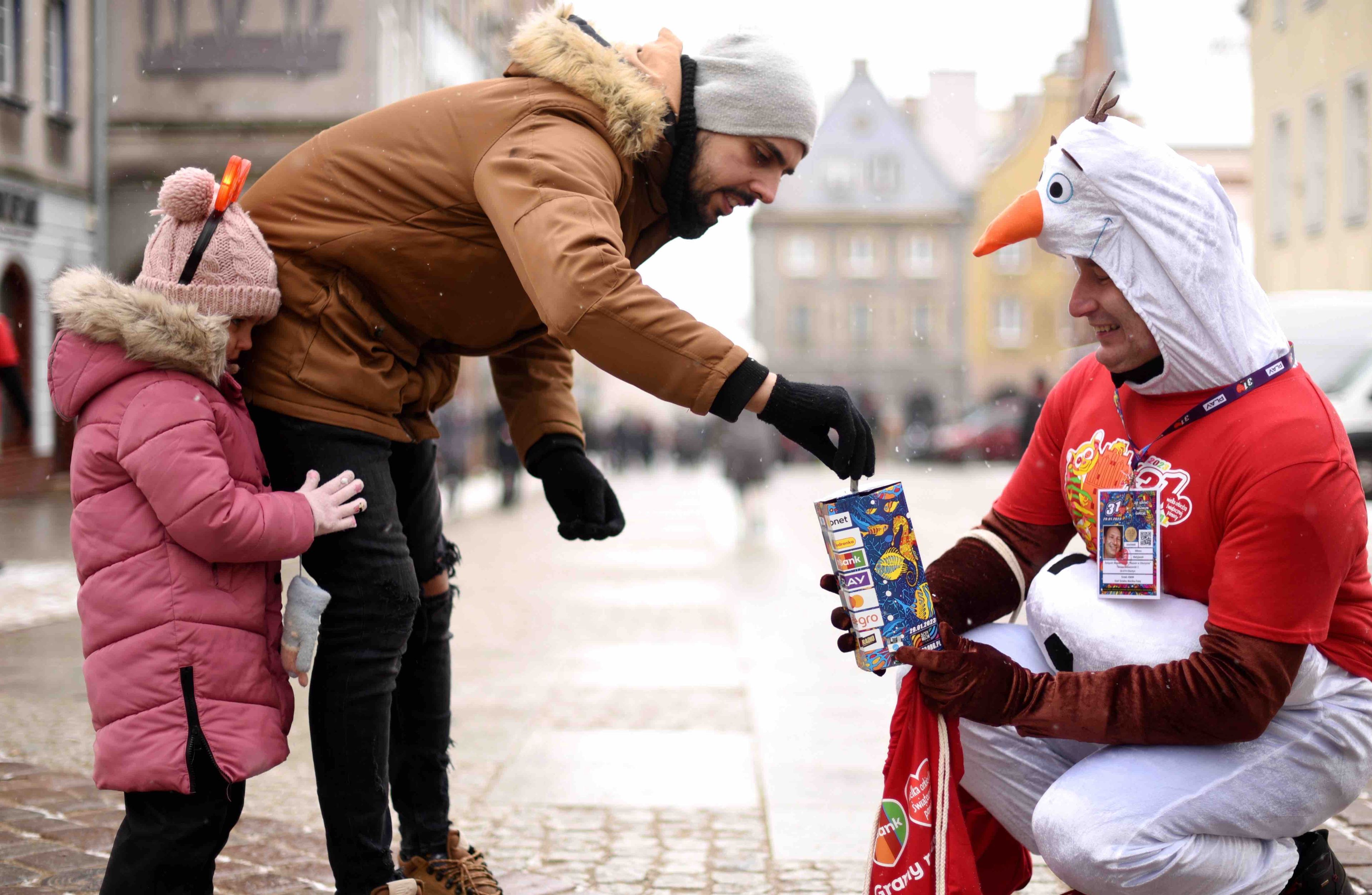 ojciec z dzieckiem wkładają pieniądze do puszki WOŚP, którą trzyma przebrany za ptaka wolontariusz