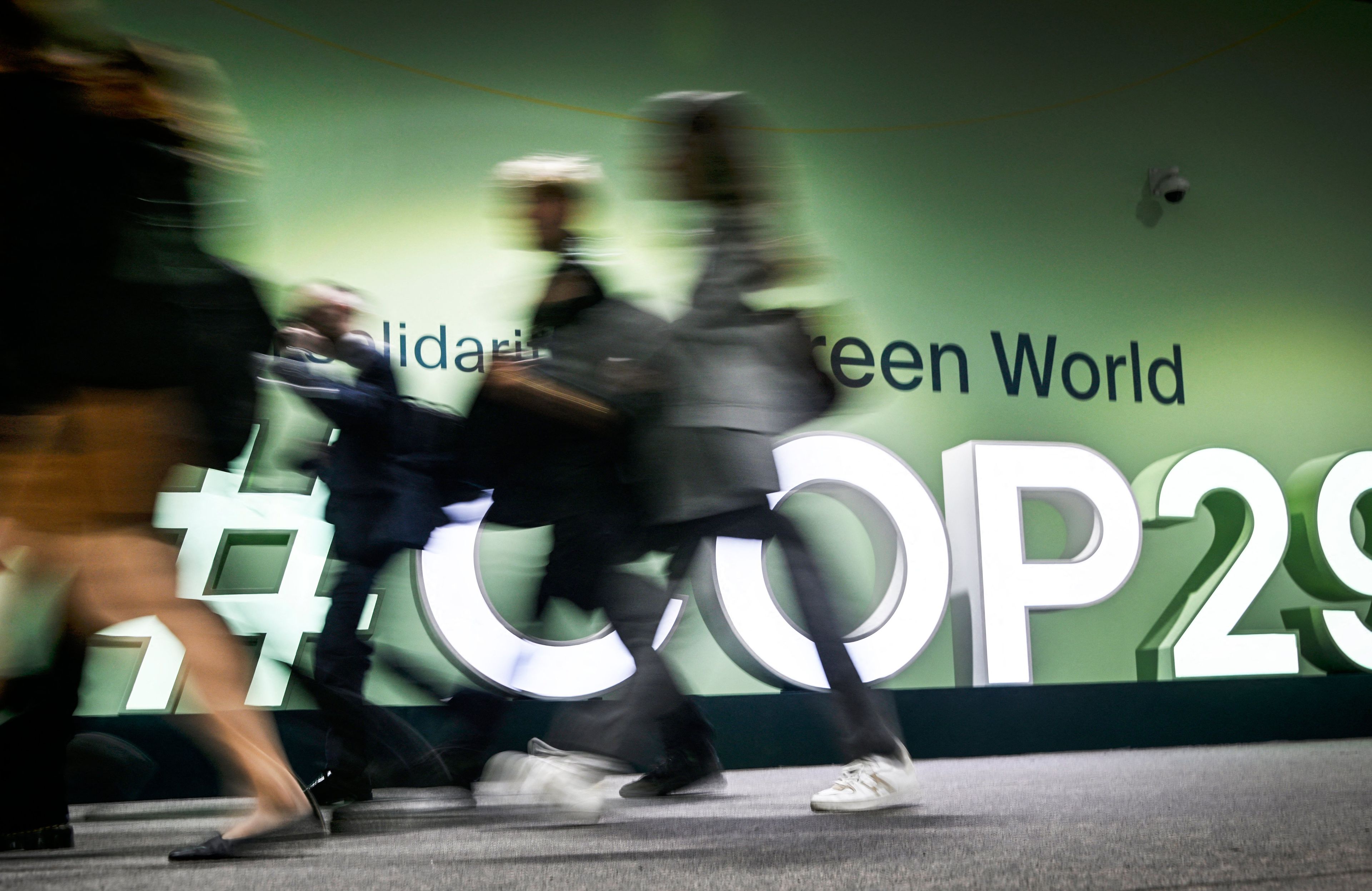 Zdjęcie przedstawia sylwetki osób na tle wielkiego napisu COP29