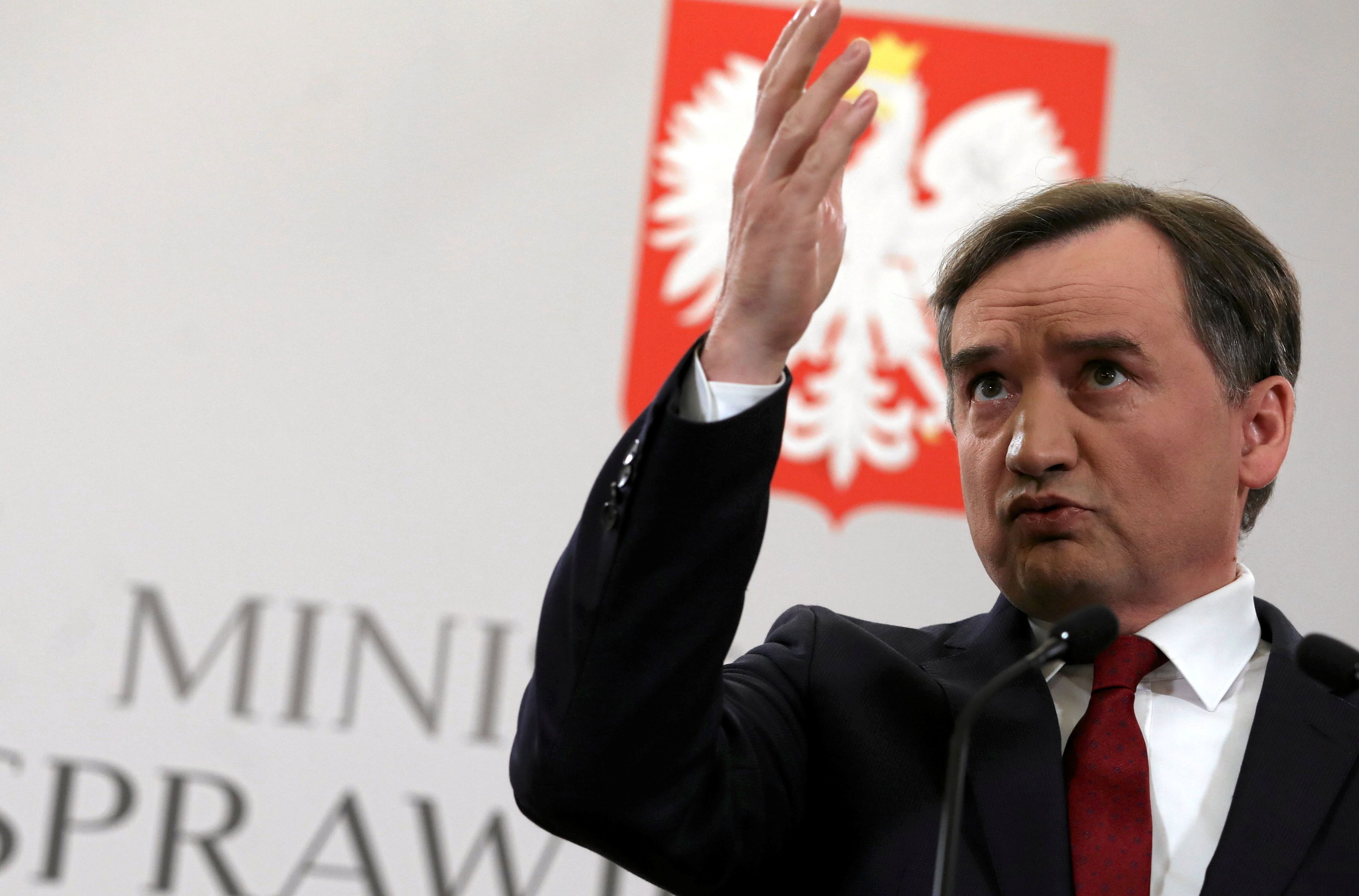 Zbigniew Ziobro z uniesioną ręką na tle logo ministerstwa sprawiedliwości