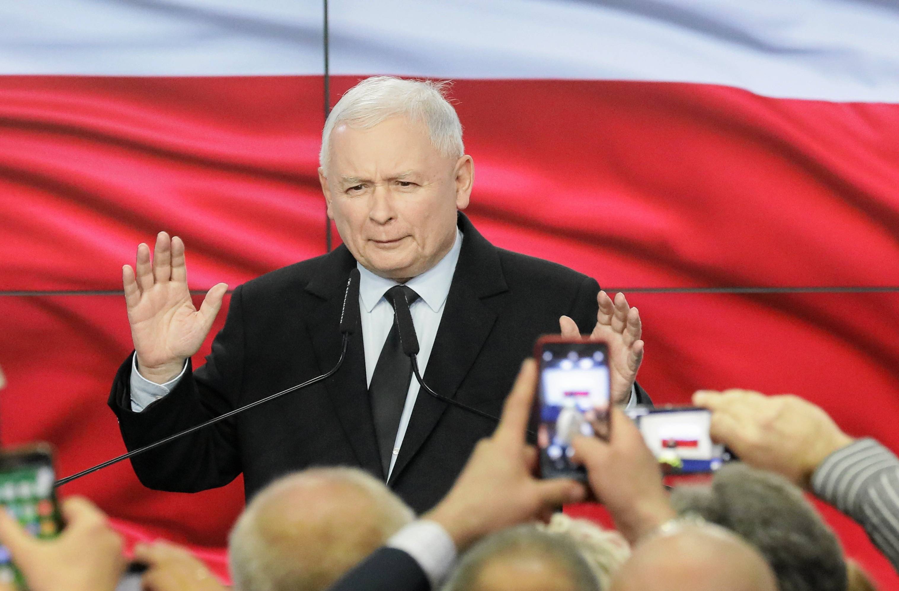 Jarosław Kaczyński przed tłumem zwolenników podczas wieczory wyborczego. Za nim na ekranie wyświetlana jest flaga Polski