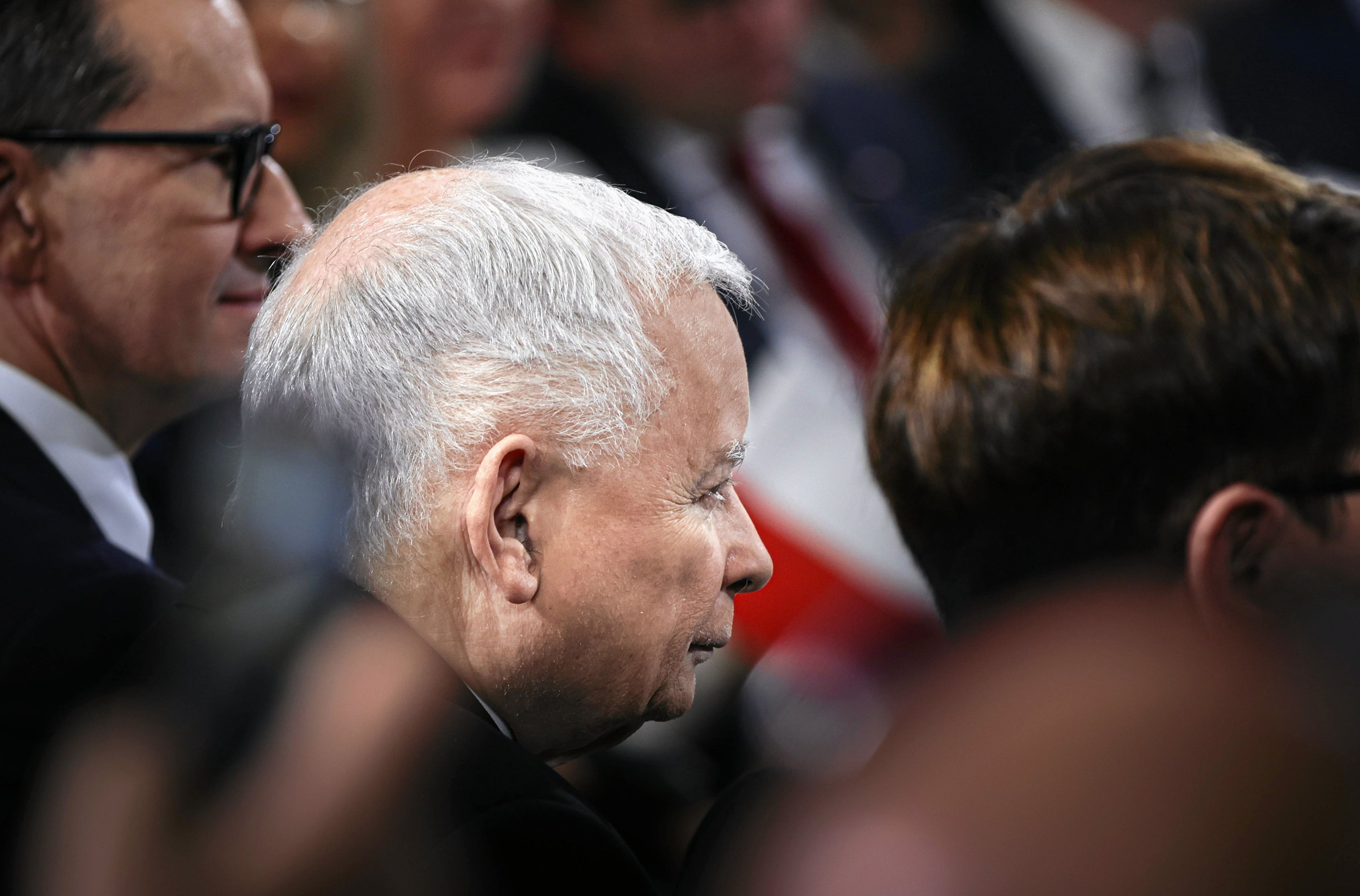 Siedzą w rzędzie: Mateusz Morawiecki, Jarosław Kaczyński i Beata Szydło. Duże zbliżenie twarzy, ostrość zdjęcia skoncentrowana na Kaczyńskim. PiS