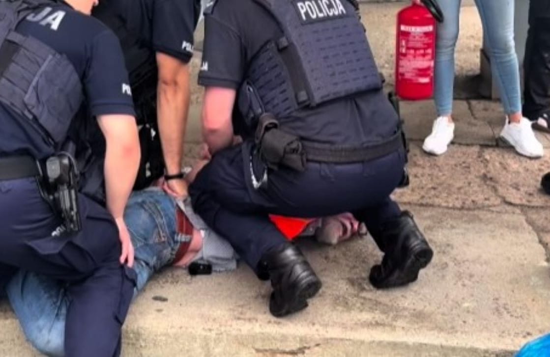 Paweł Kasprzak na ziemi, przyciśnięty przez policjantów