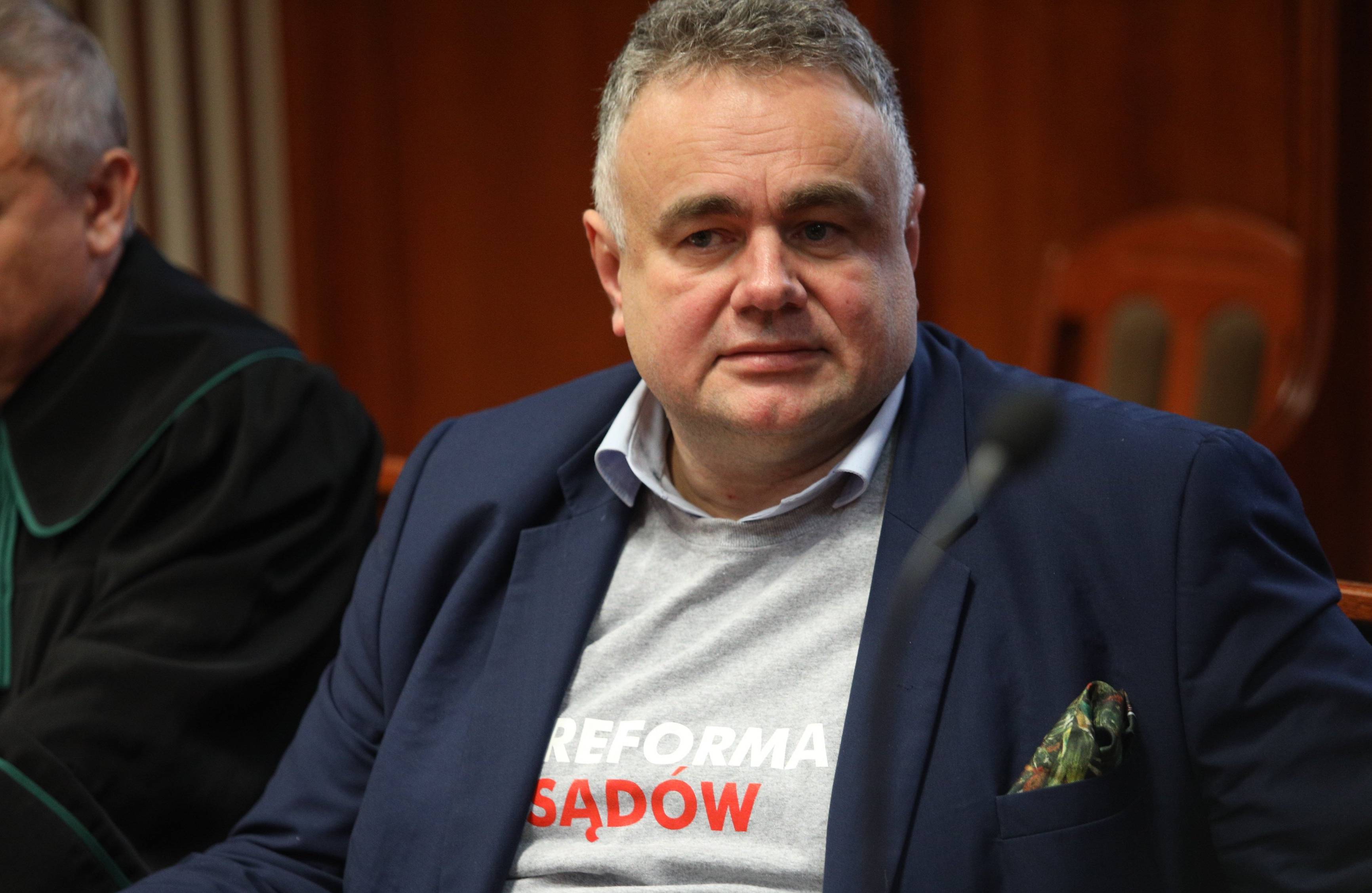 Tomasz Sakiewicz w koszulce z napisem Reforma sądów siedzi na sali sądowej obok adwokata