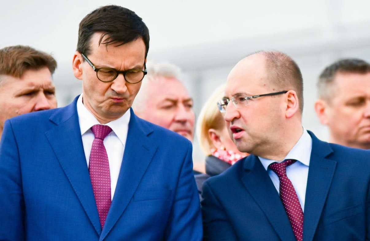 Premier Mateusz Morawiecki ze zirytowaną miną słucha, co mówi do niego stojący po lewej Adam Bielan.