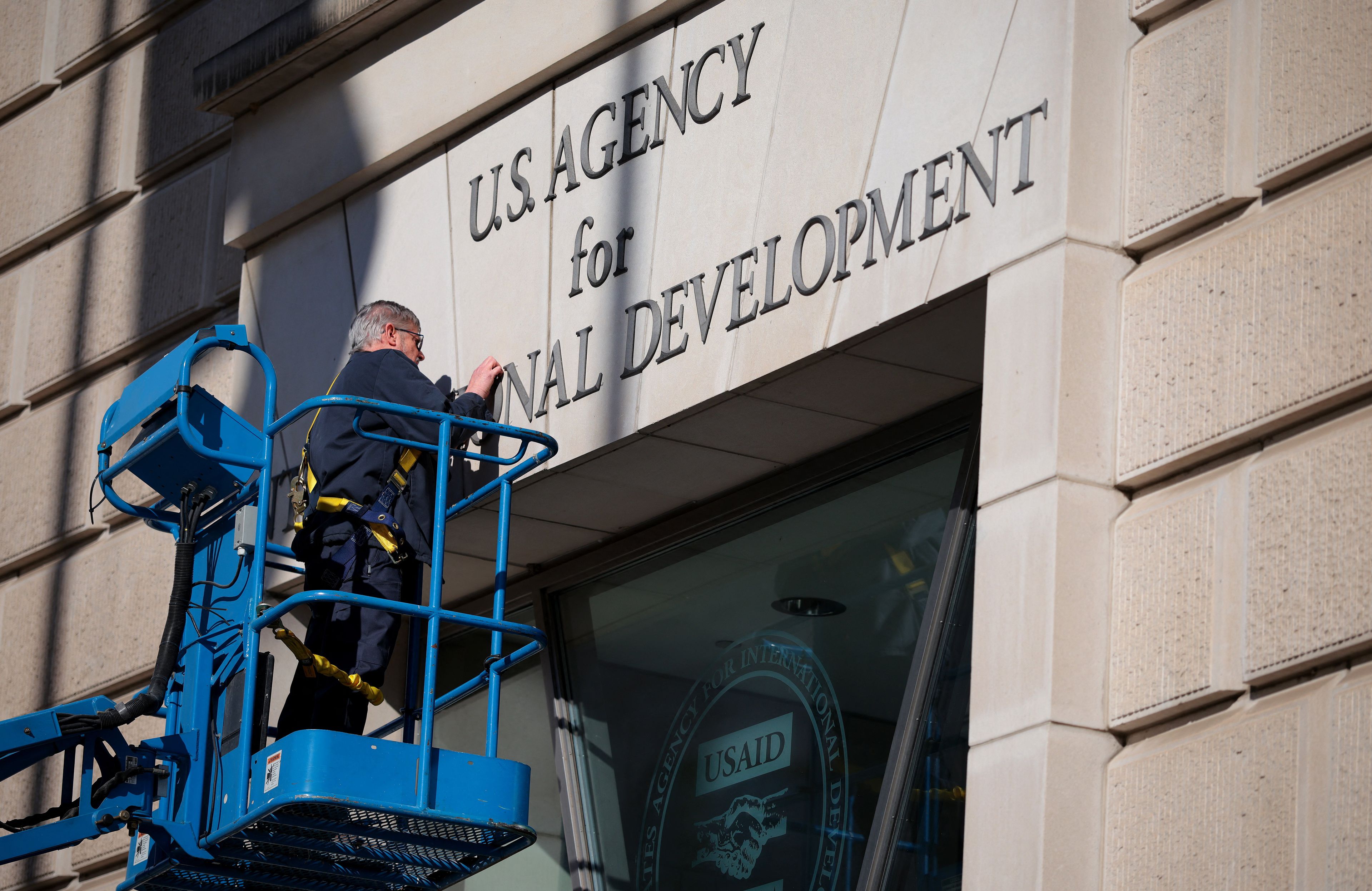 Robotnik na wysięgniku usuwa napis nad wejściem do USAID