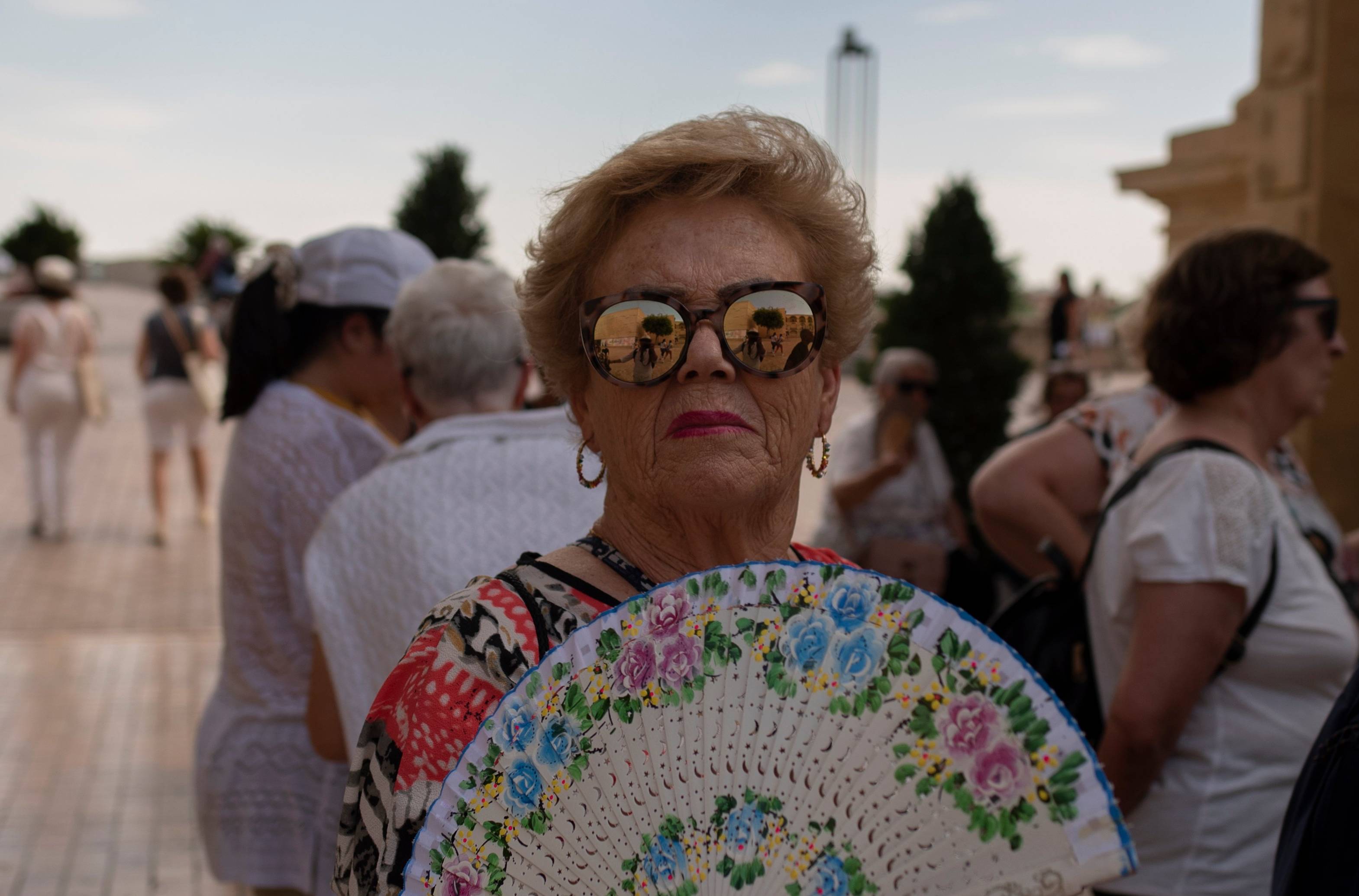 starsza pani w przeciwsłonecznych okularach i z wachlarzem na tle tłumu