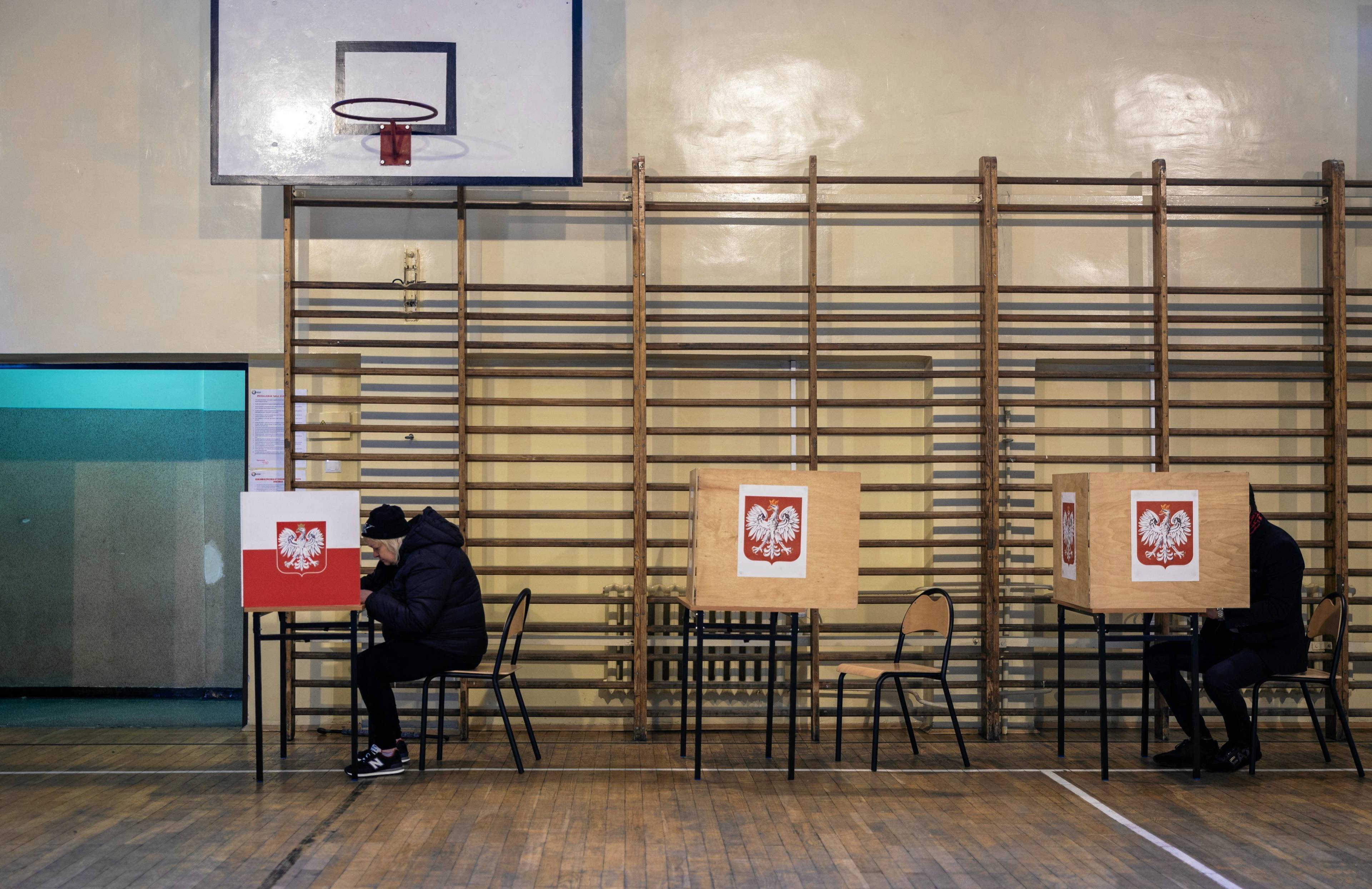 sala gimnastyczna wszkole, przy stolku zasłonięta zastawką osoba zaznacza swój wybór na karcie do głosowania