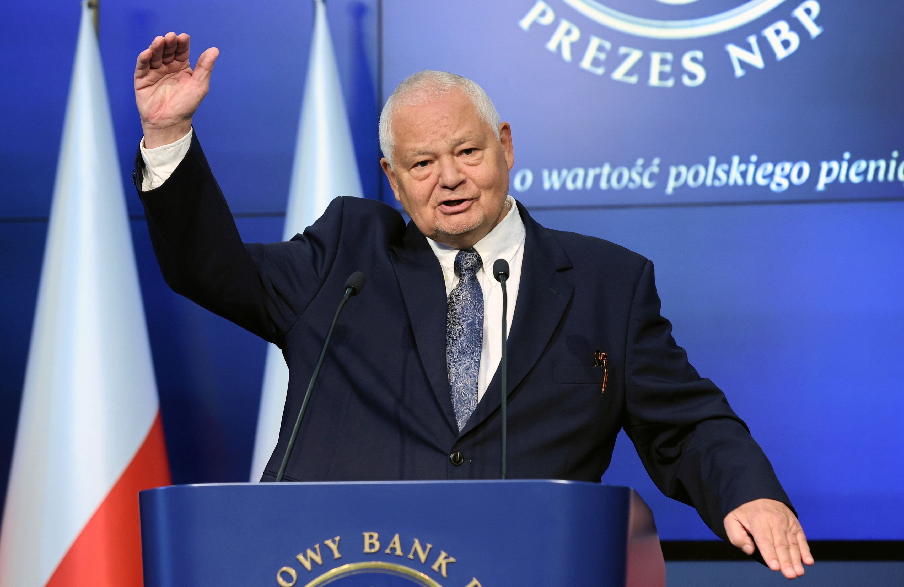 Prezes NBP Adam Glapiński podczas konferencji prasowej podnosi rękę, gestykulując