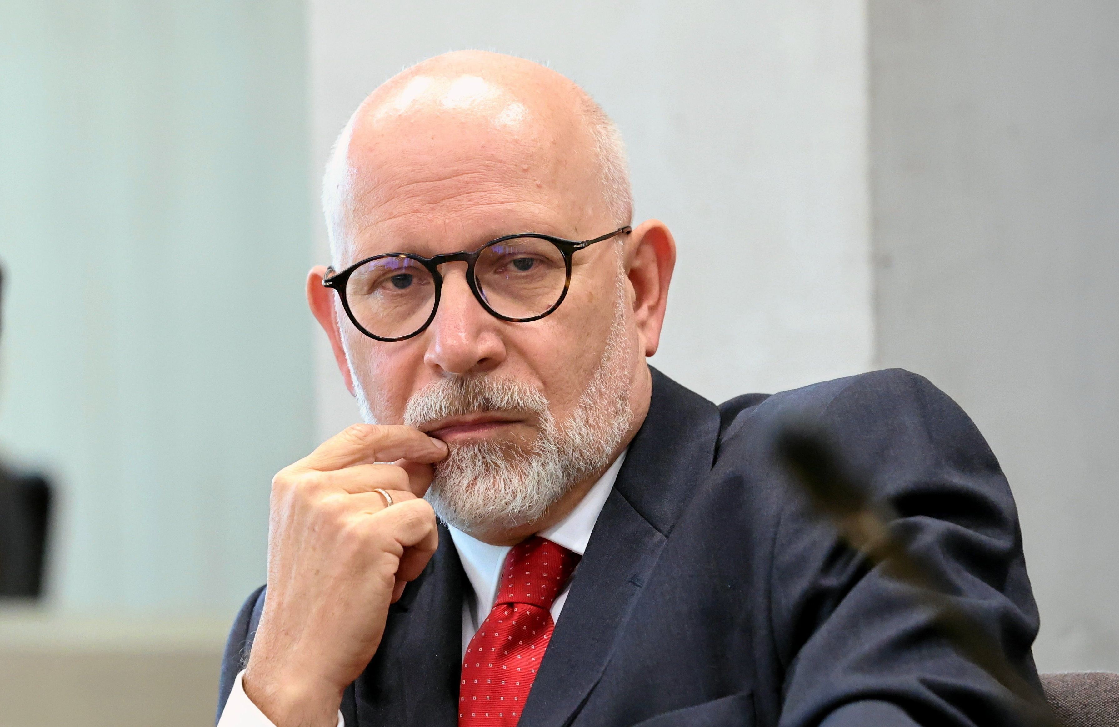 Starszy łysy mężczyzna w okluarach. Gest dłoni sugeruje namysł