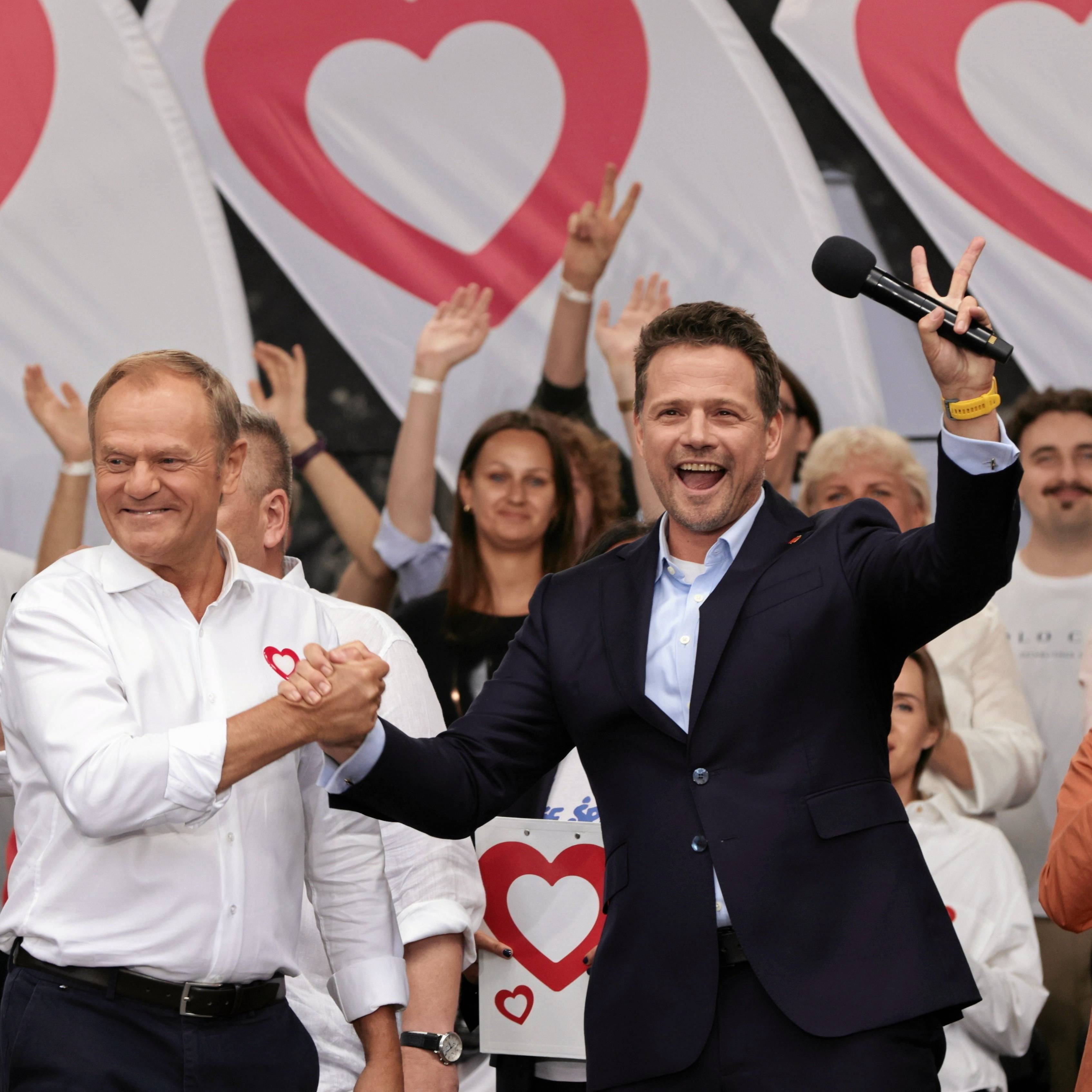 Donald Tusk i Rafał Trzaskowski podają sobie ręce w geście radości, Trzaskowski pokazuje przy tym gest zwycięstwa