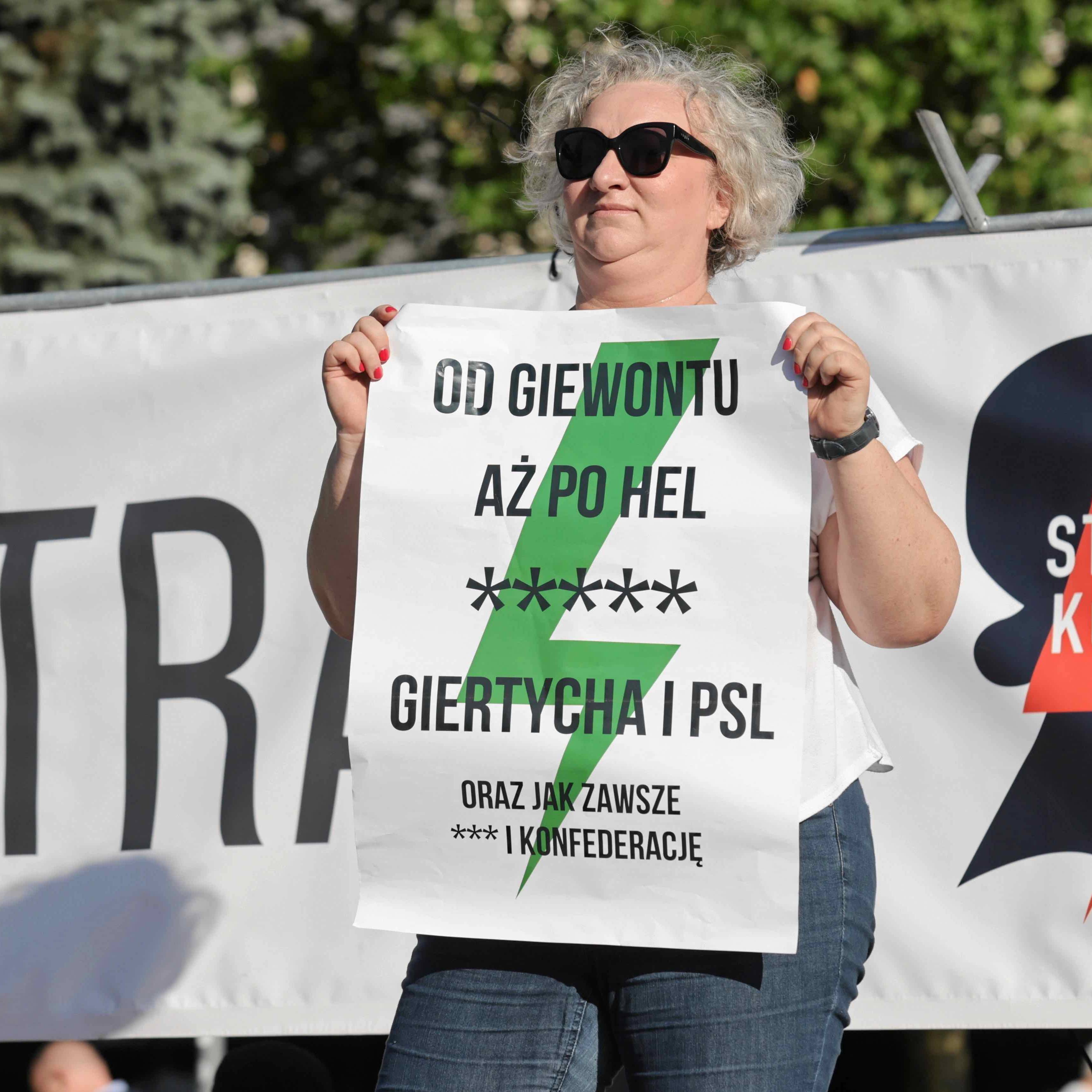 Kobieta stoi na scenie podczas demonstracji trzymając plakat z napisem Od Giewontu aż po Hel [pięć gwiazdek] Giertycha i PSL