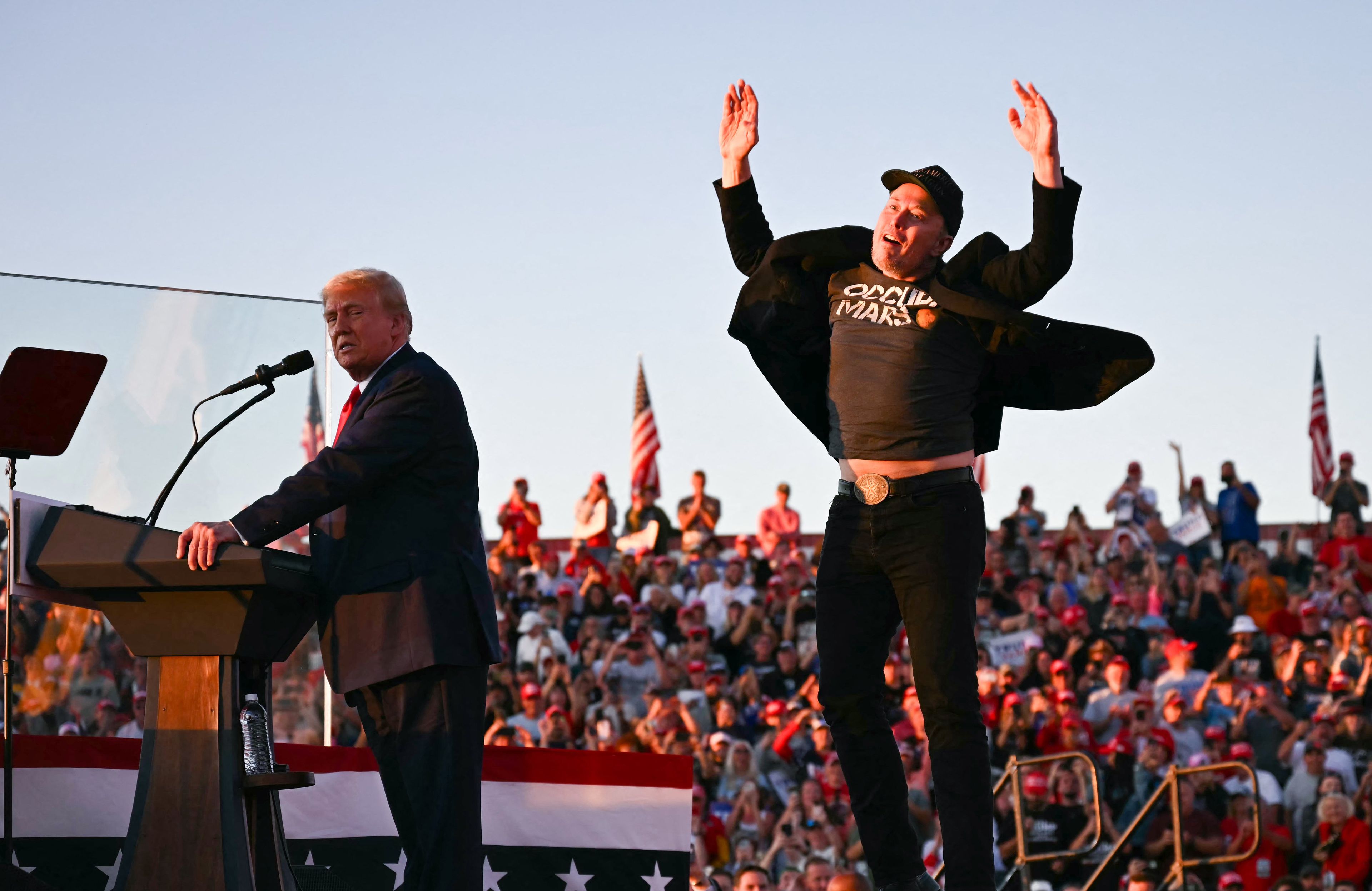 Tesla CEO Elon Musk (R) jumps on stage as he joins former US President and Republican presidential candidate Donald Trump during a campaign rally at site of his first assassination attempt in Butler, Pennsylvania on October 5, 2024.