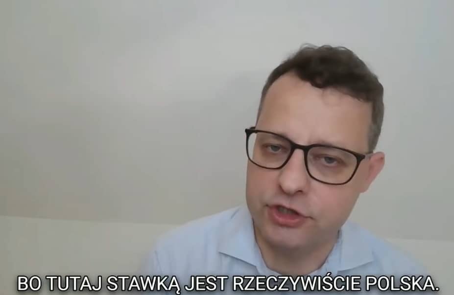 Mezczyzna w czarnych okularach i niebieskiej koszuli (Marcin Romanowski) mowi do internetowej kamery. Na dole ekranu napis "Bo tutaj stawką jest rzeczywiście Polska"