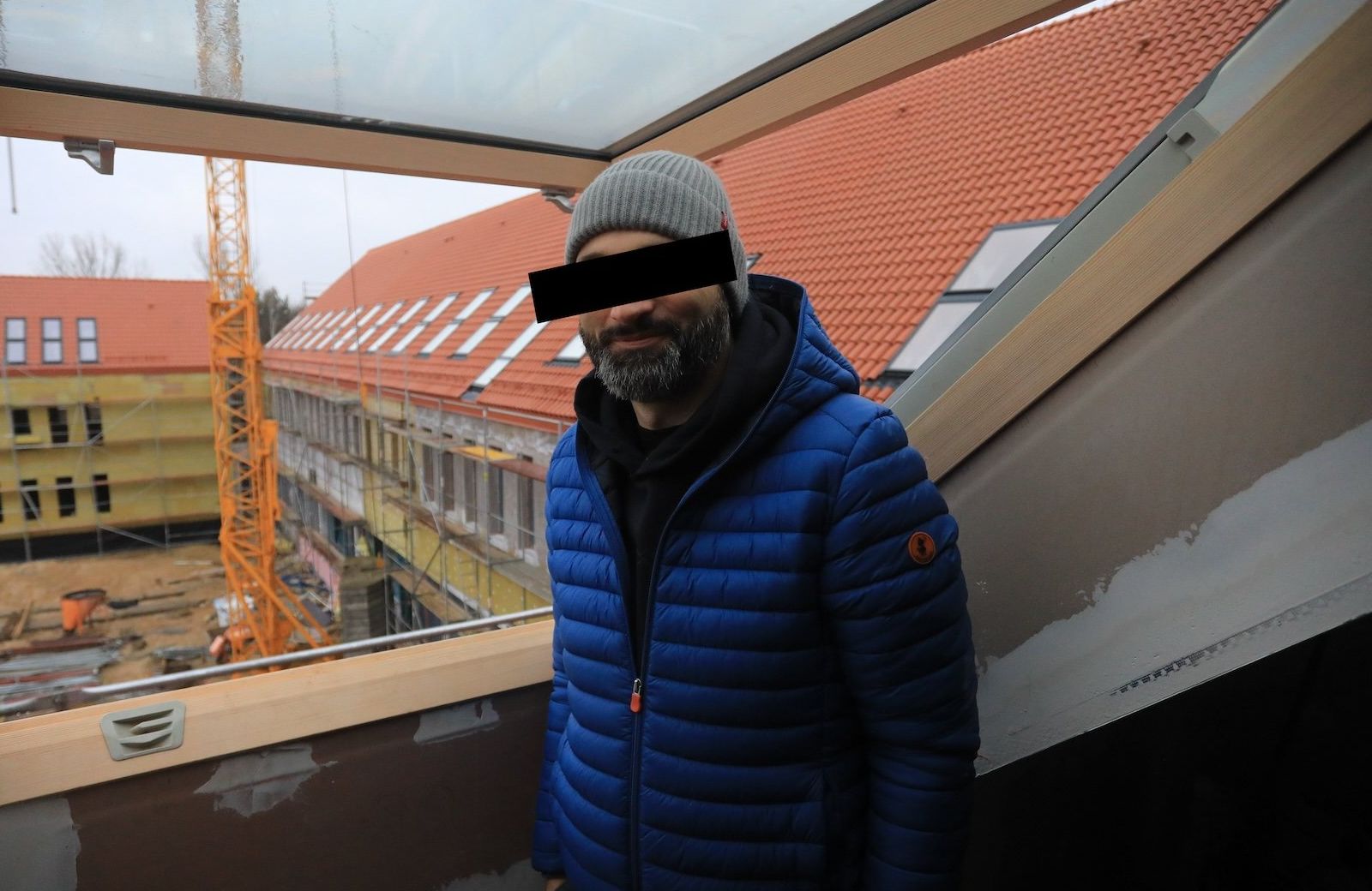 Ksiądz Michał O. w niebieskiej kurtce puchowej i szarej czapce pozuje w ośrodku Archipelag, który buduje Fundacja Profeto