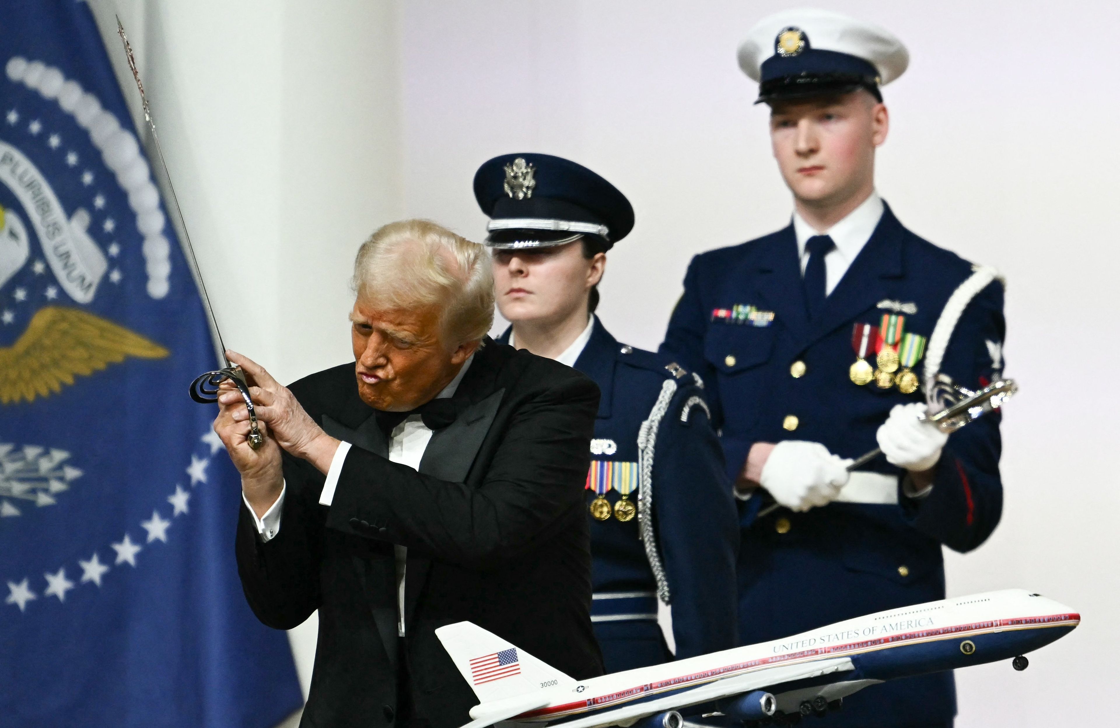 Donald Trump wymachuje szablą nad tortem w kształcie Air Force One, z tyłu żołnierze w galowych mundurach