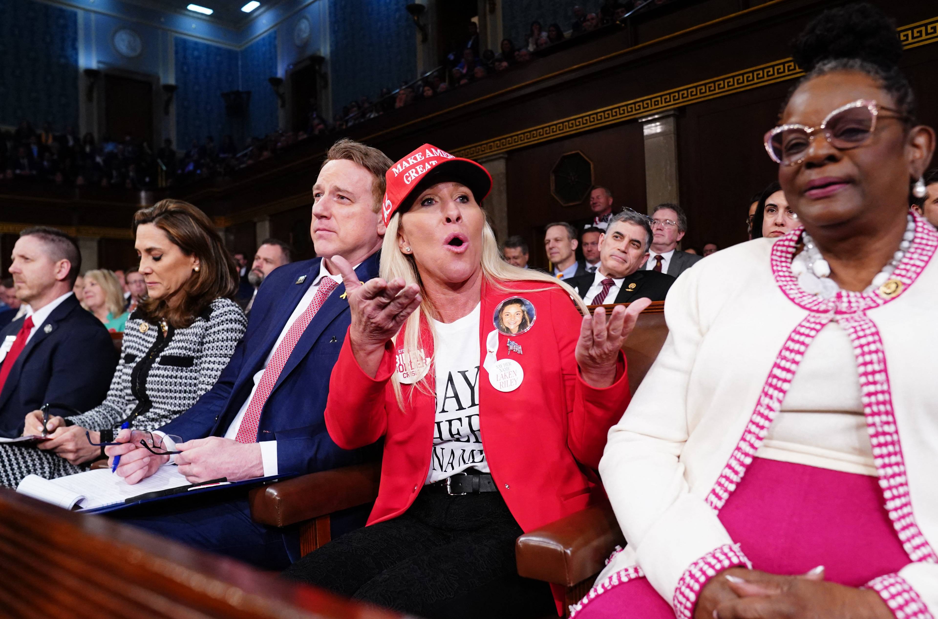 Kobieta ubrana na czerwono z czerwoną czapką na głowie krzyczy siedzie w ławach amerykańskiego kongresu
