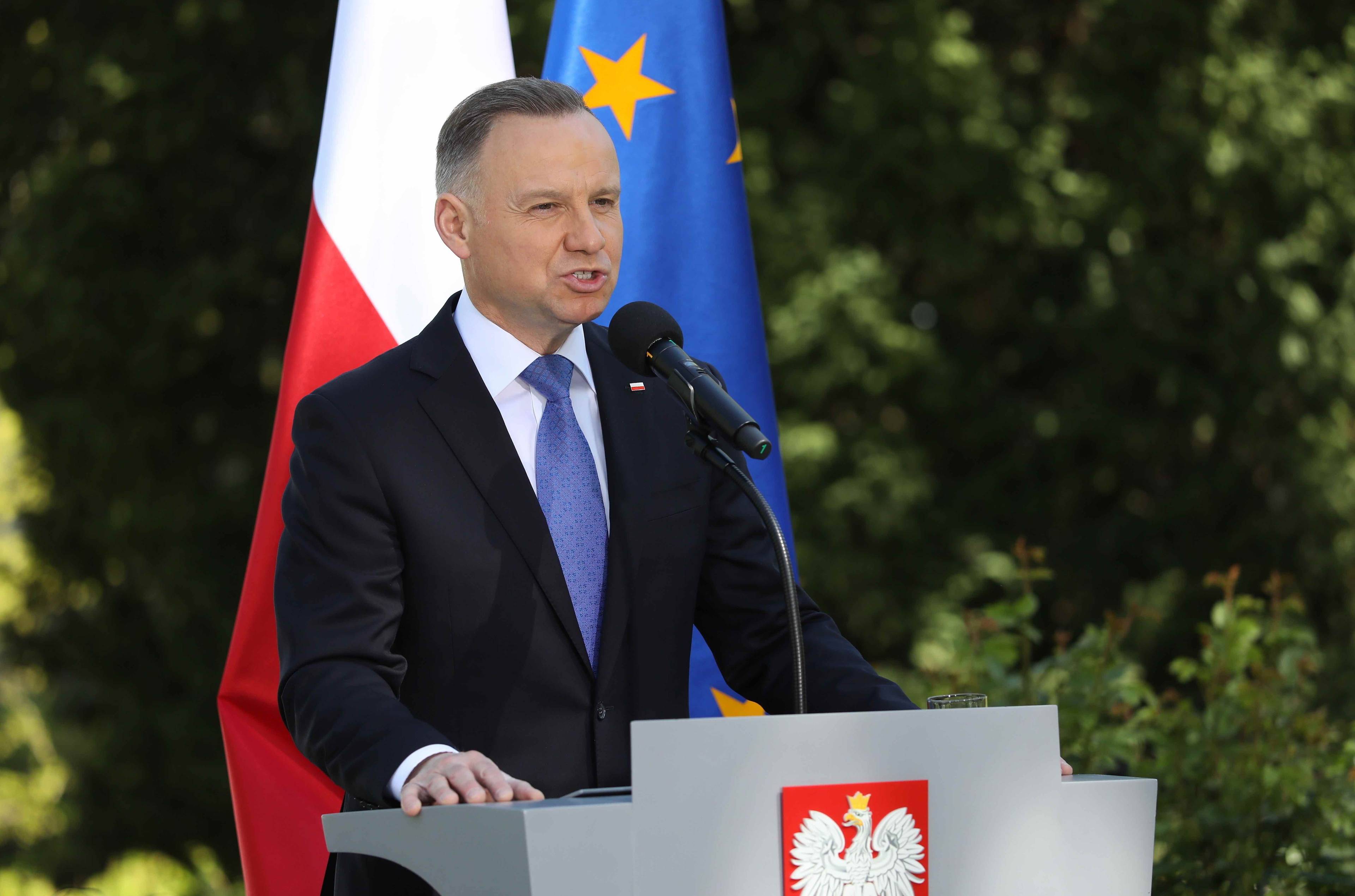 Prezydent Andrzej Duda przemawia w ogrodzie za mównicą z polskim godłem.