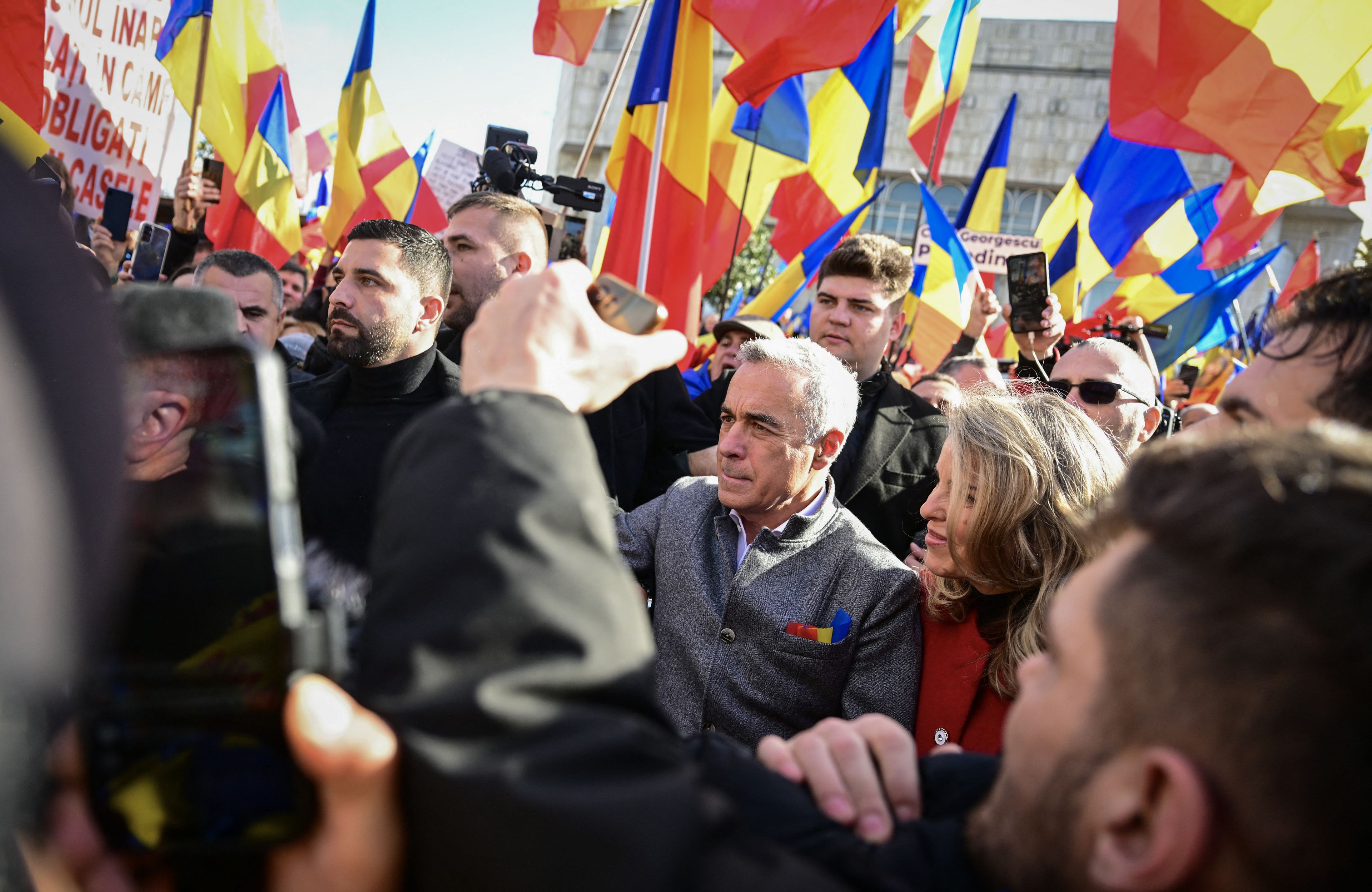 Kandydat na prezydenta Calin Georgescu przechodzi przez tłum, w tle liczne rumuńskie flagi