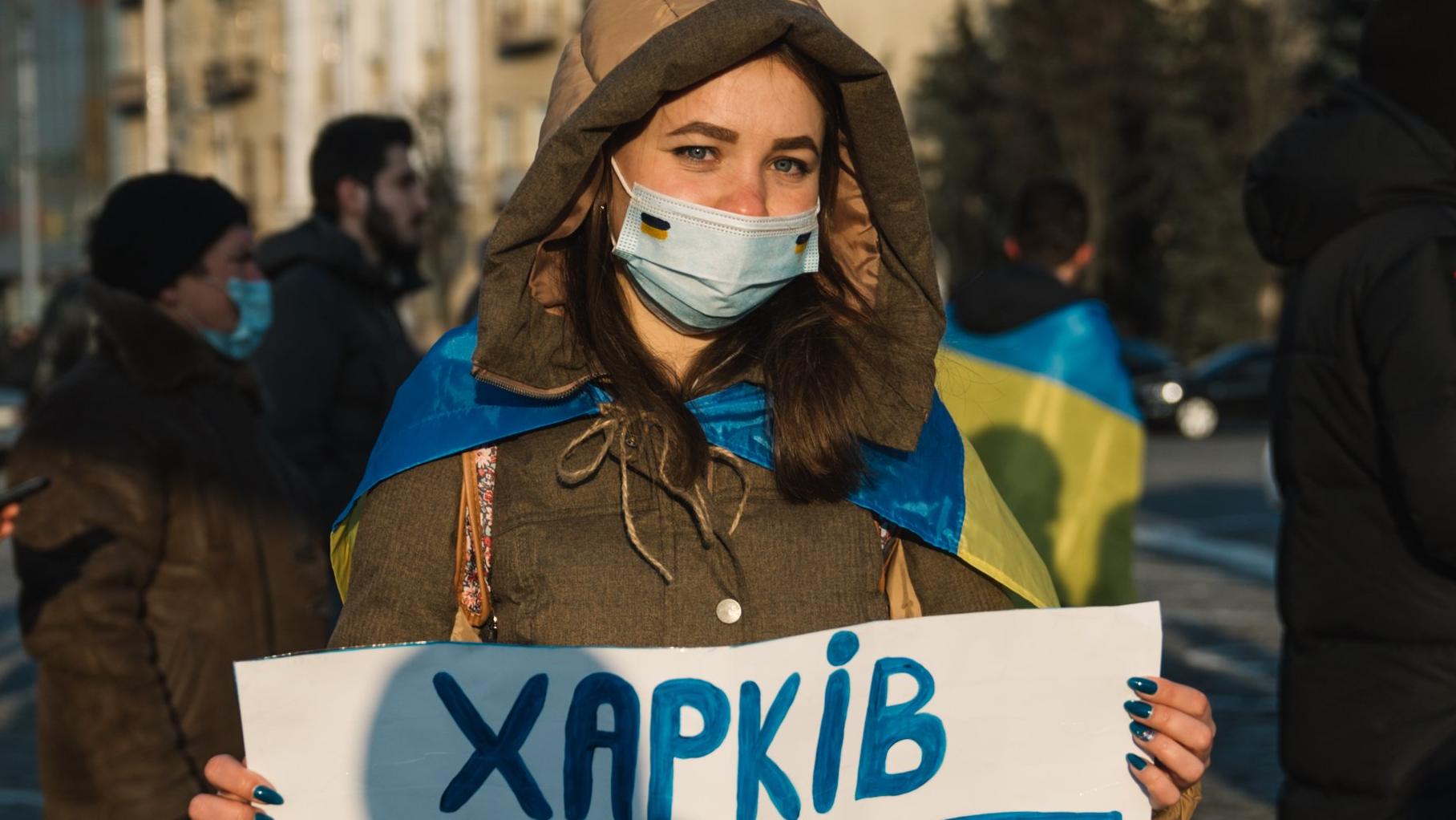 Ołesia Dekusz w zimowej kurtce i maseczce trzyma plakat "Charkiv Ukraina"