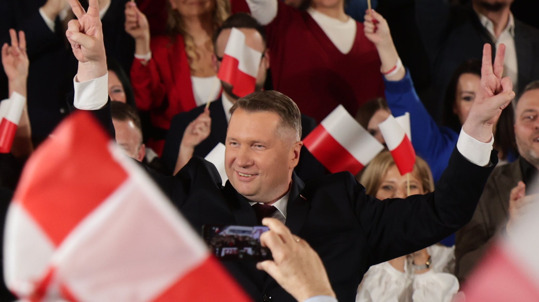 Przemysław Czarnek unosi ręce w goście zwycięstwa, wokół dużo ludzi i biało-czerwonych flag