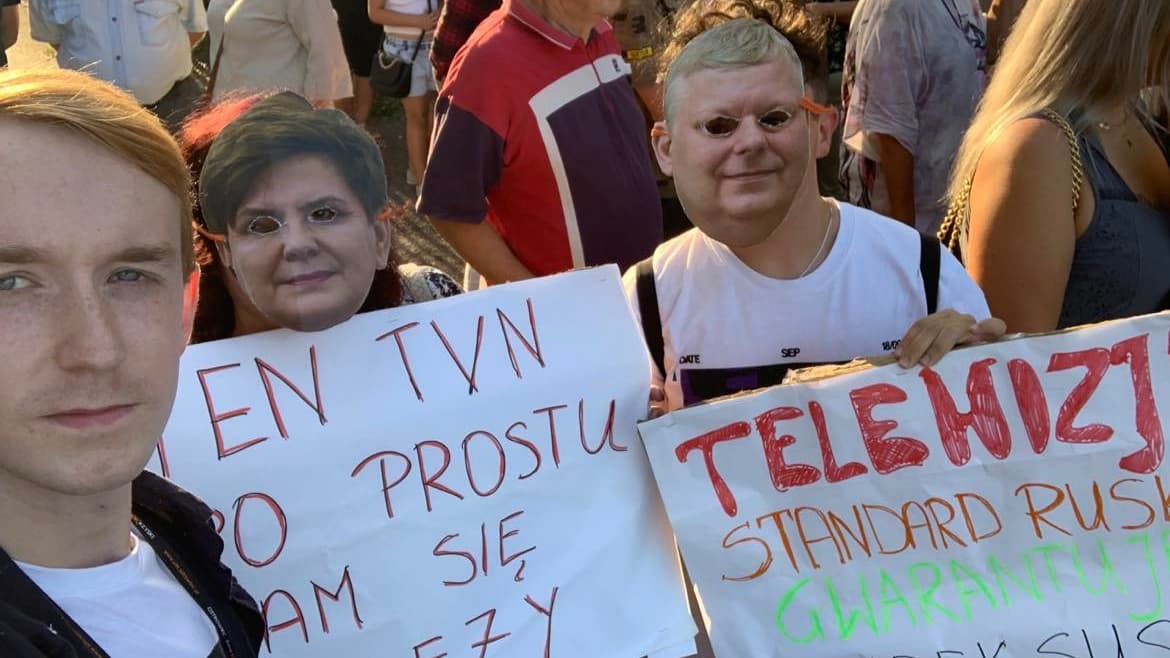 Ludzie z maskami twarzy Beaty Szydło i Marka Suskiego trzymają transparent "Ten TVN nam się po prostu nalezy"