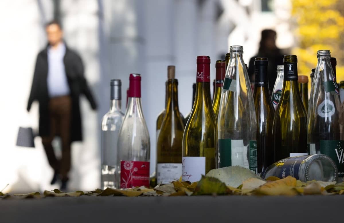 Pedestrian pass by empty bottles of alcohol on a sidewalks, in Paris, on November 22, 2023. (Photo by JOEL SAGET / AFP)