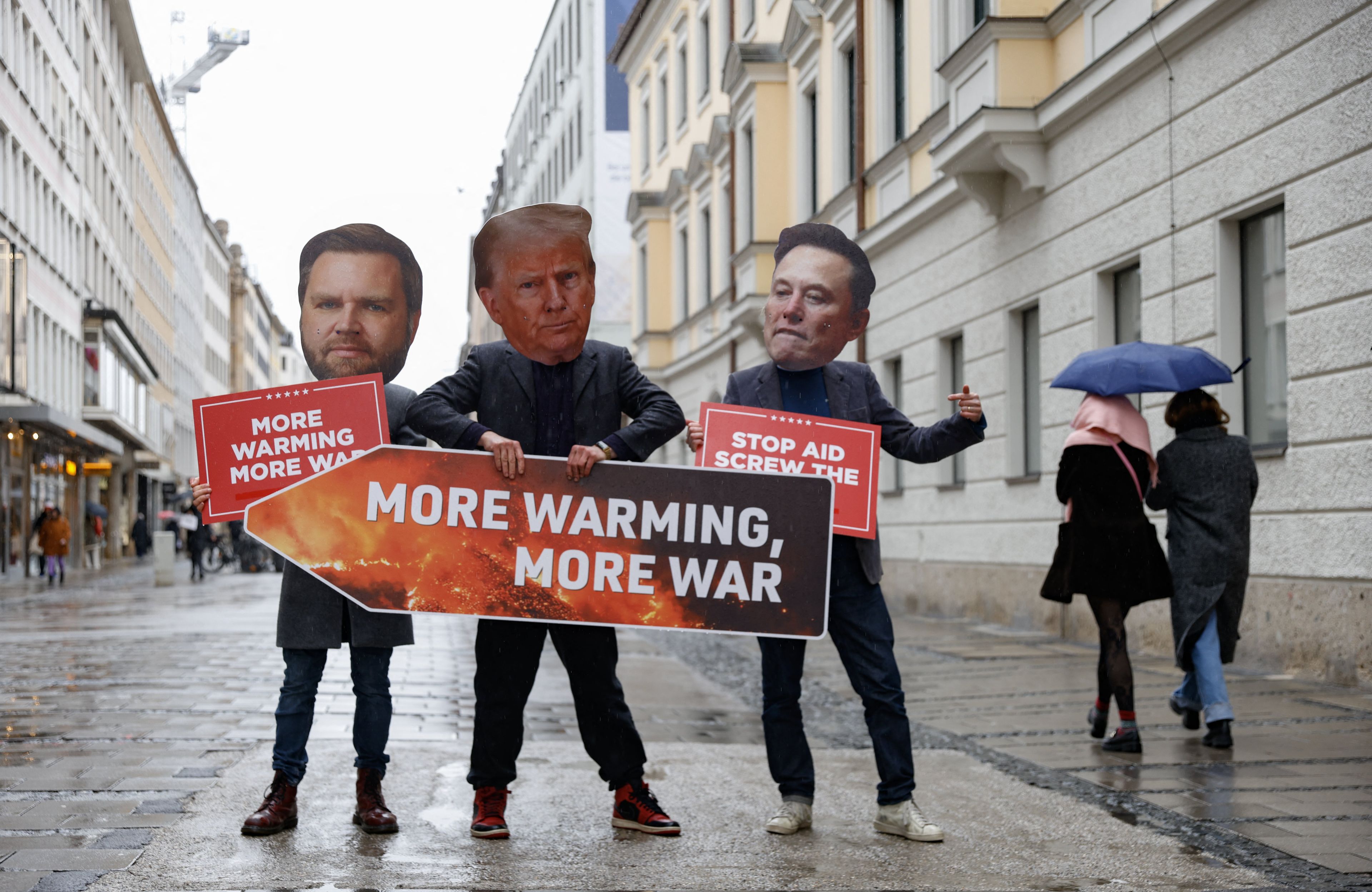 trzy osoby z maskami Trumpa, Vancea i Muska, trzymają napisa more warming more war