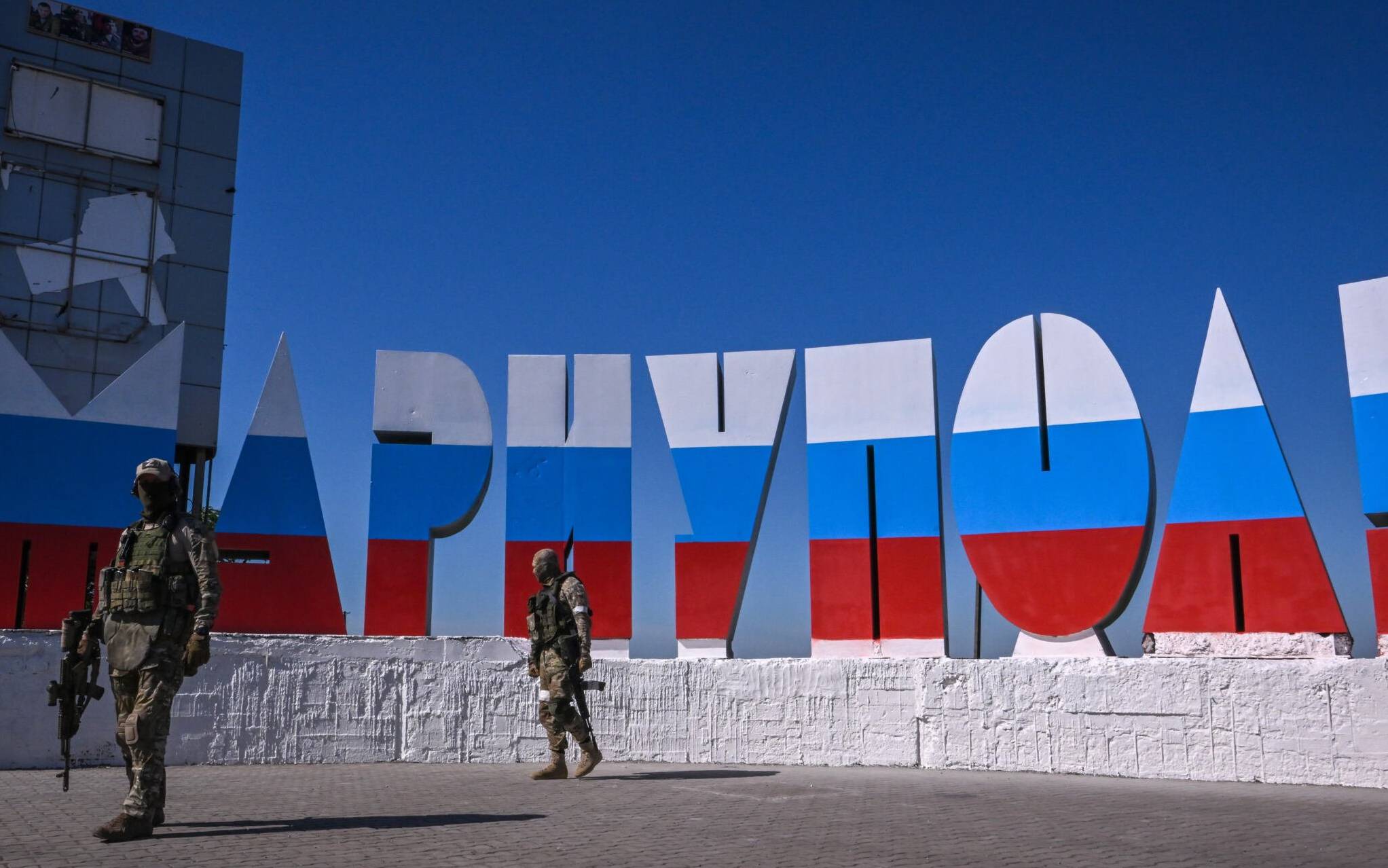 Russian servicemen walk near the welcome sign "Mariupol", which has been painted in Russian flag colours, at the entrance of Mariupol on June 12, 2022, amid the ongoing Russian military action in Ukraine. (Photo by Yuri KADOBNOV / AFP)