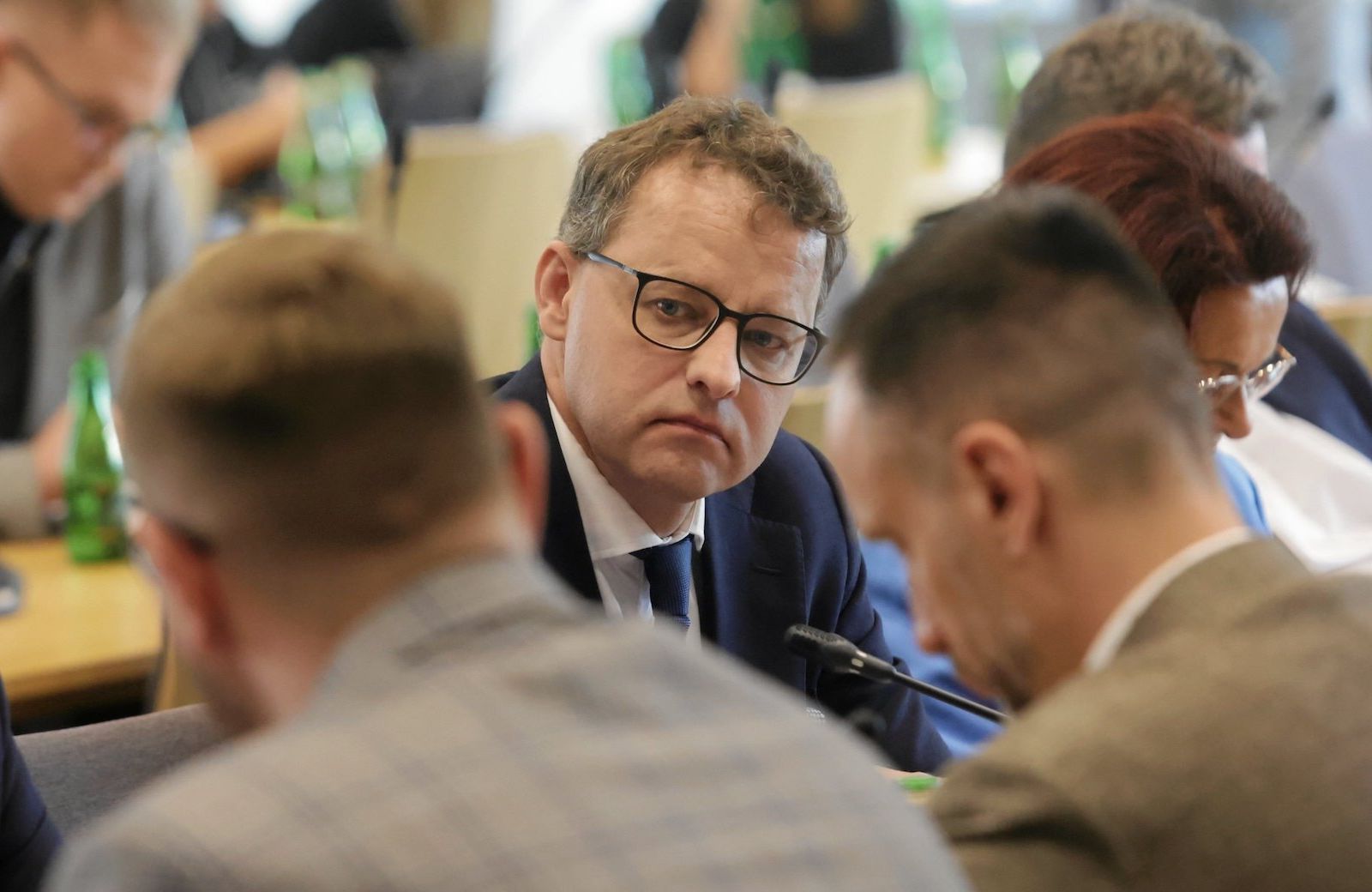 Marcin Romanowski podczas prac sejmowej komisji etyki poselskiej. Spogląda w kamerę, na pierwszym tle odwrócenie plecami inni politycy