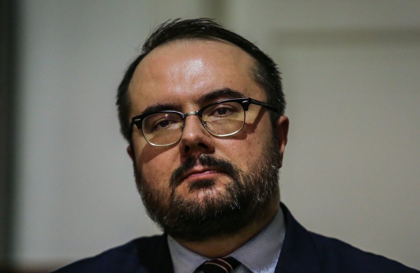 Portret podsekretarza stanu w MSZ Pawła Jabłońskiego: mężczyzna o ciemnych włosach i ciemnym zaroście, w okularach, twarz pucołowata. Ubrany w ciemny garnitur, jasnoniebieską koszulę i krawat w paski. W kapie marynarki przypinka z polską flagą.