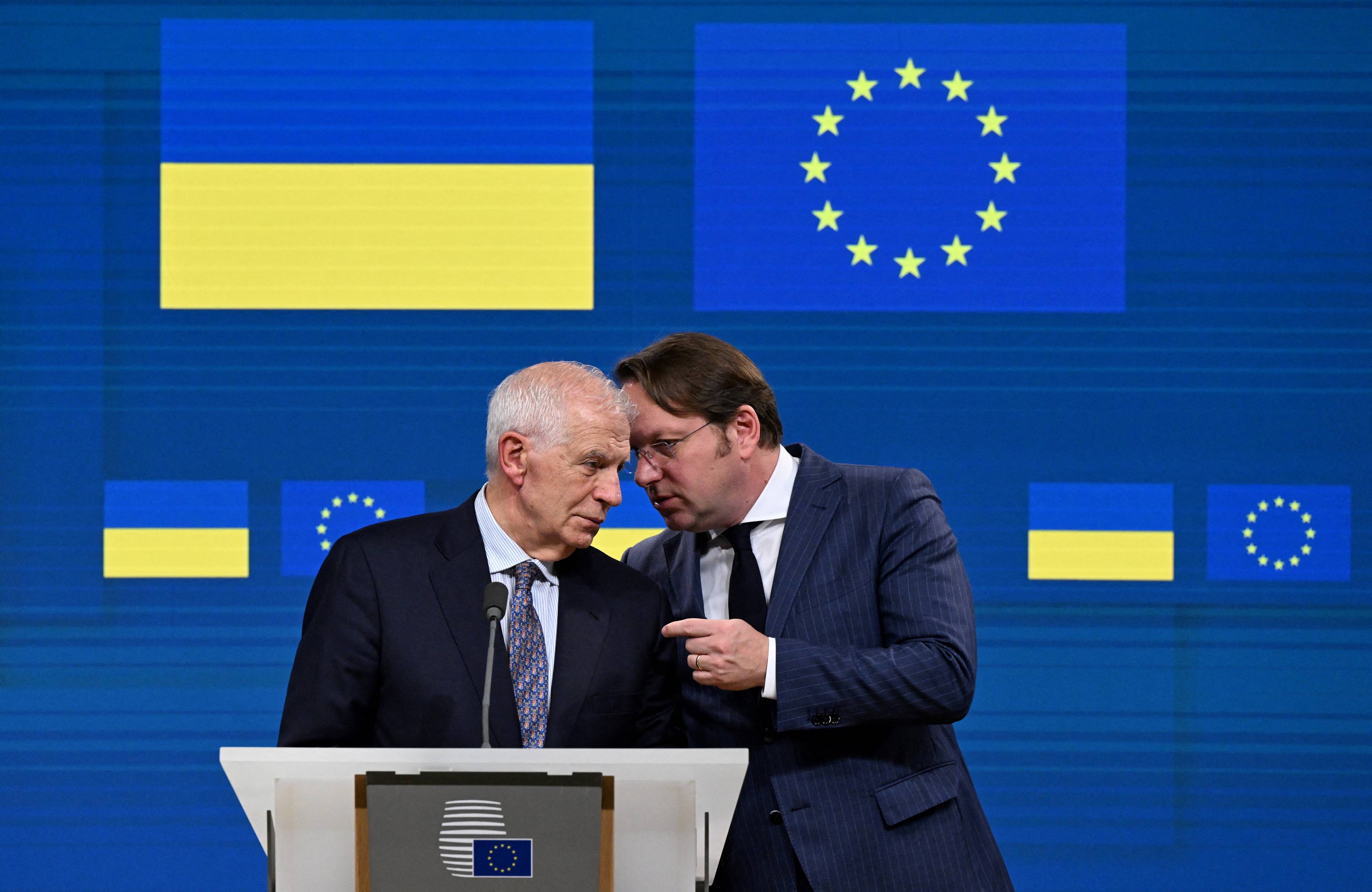 Na zdjęciu jest dwóch mężczyzn. W tle są flagi Ukrainy i Unii Europejskiej. Jeden z mężczyzn coś mówi na ucho innemu. Są to przedstawiciele Unii Europejskiej