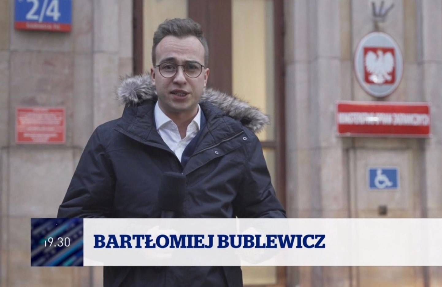 Mężczyzna w okularach, w kurtce, stoi na tle budynku ministerstwa i mówi do mikforonu. Pod spodem na pasku napis Bartłomiej Bublewicz, 19:30