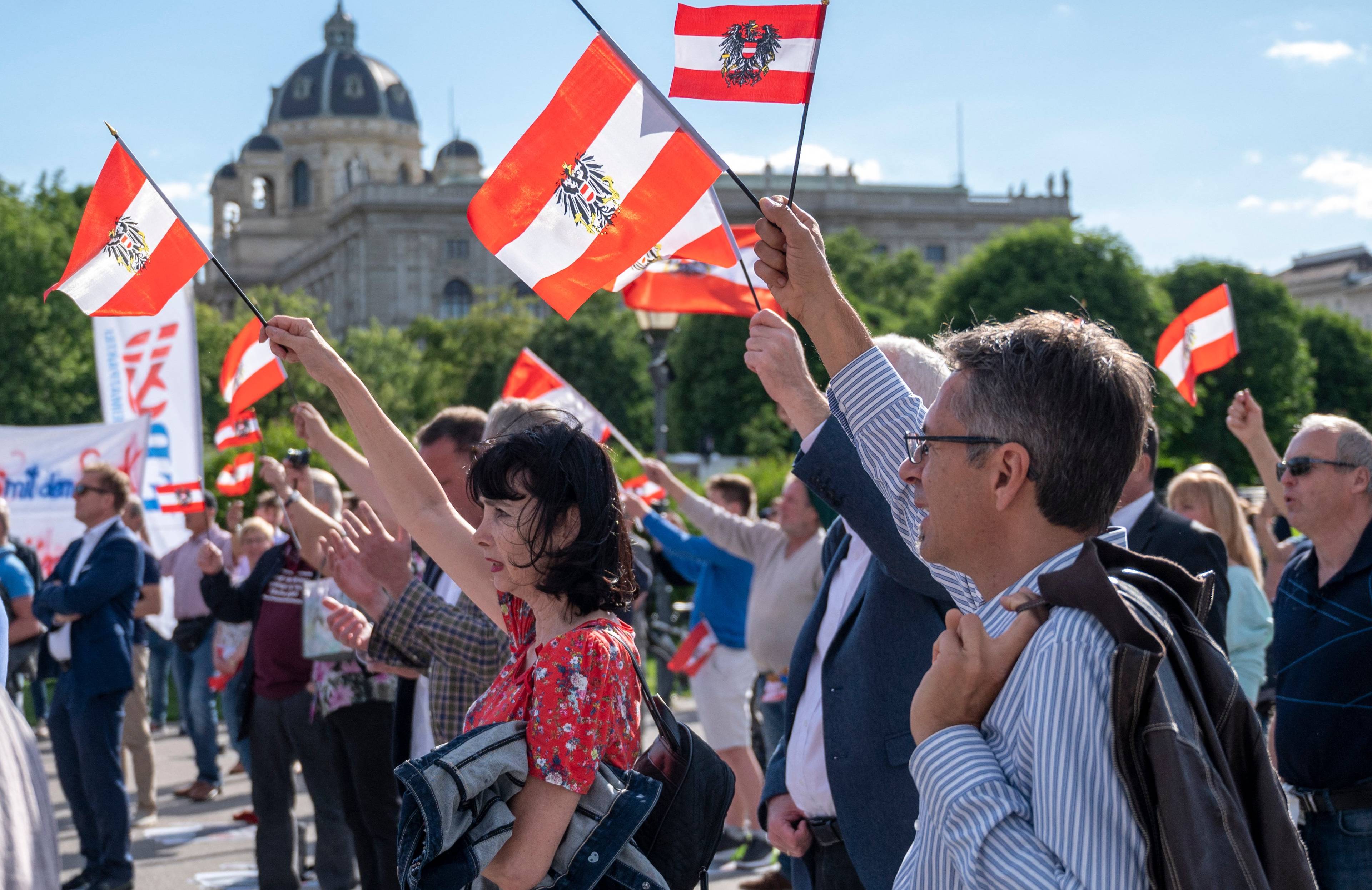 Zwolennicy FPÖ demonstrują, trzymają w wyciągniętych do góry prawych rękach austriackie flagi