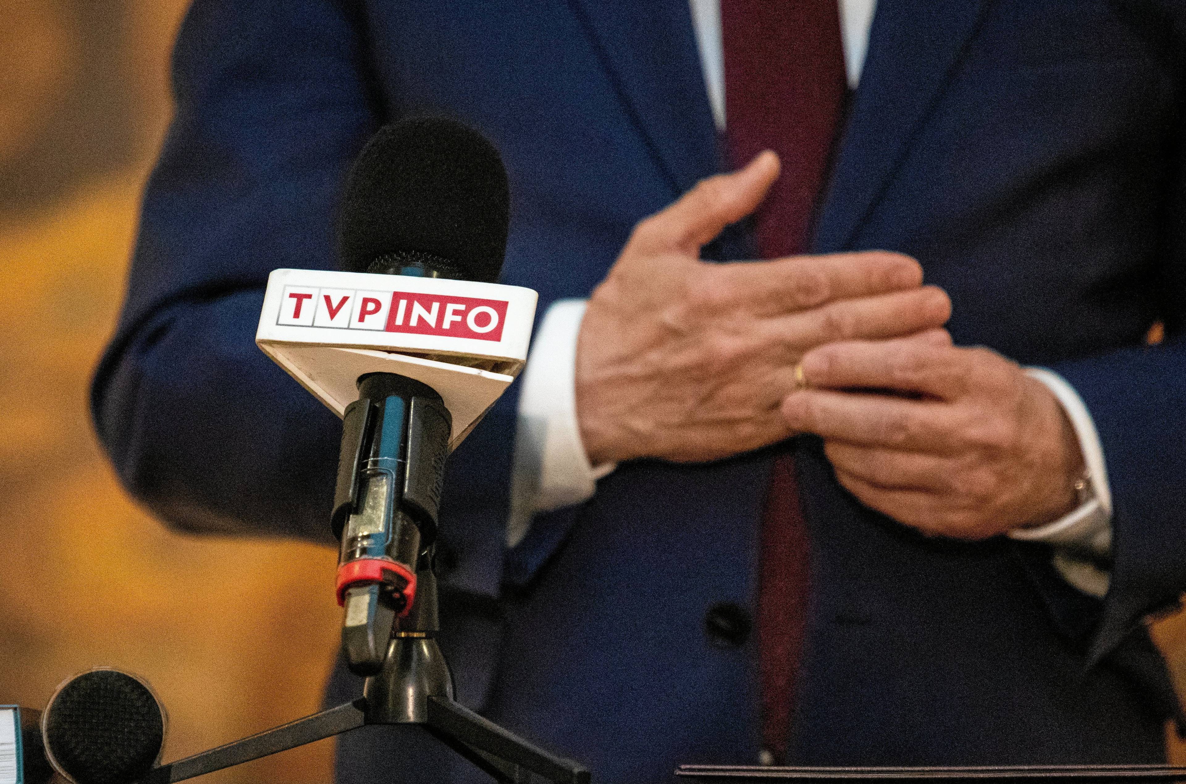 Mikrofon z napisem TVP Info, w tle dłonie mężczyzny w garniturze