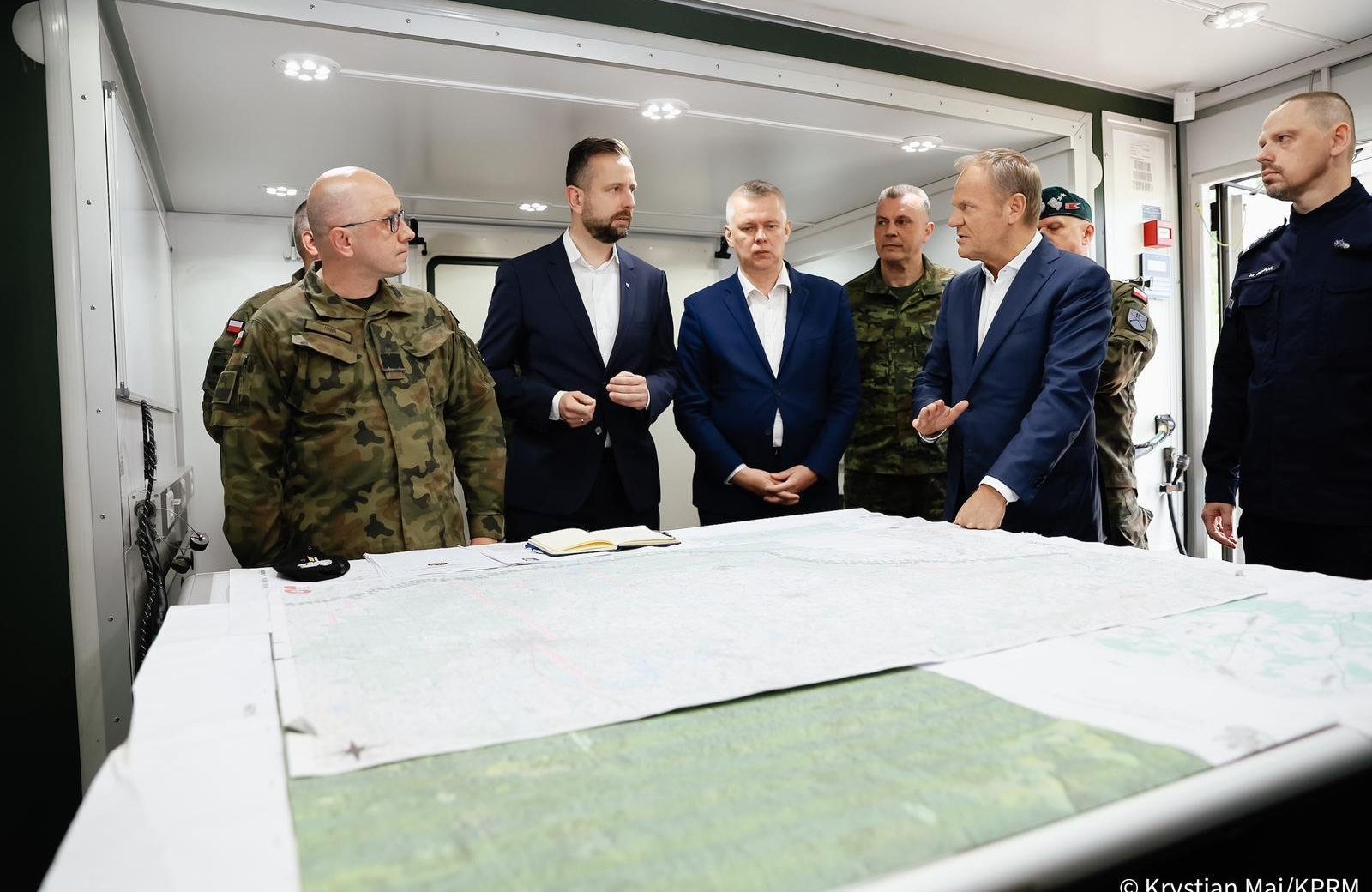 Politycy w marynarkach i wojskowi w mundurach rozmawiają nad mapą sztabową położoną na stole