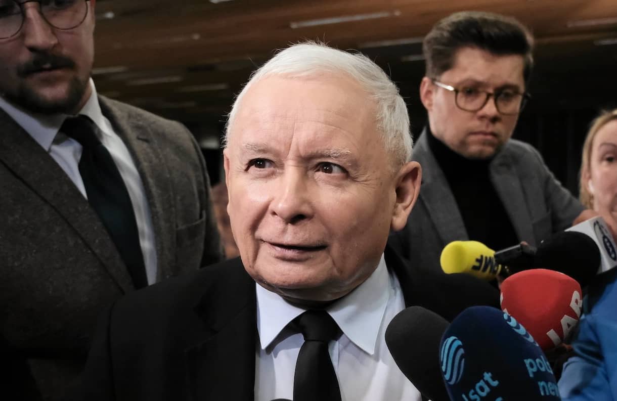 Jarosław Kaczyński otoczony przez dziennikarzy. Uśmiecha się do kamery.