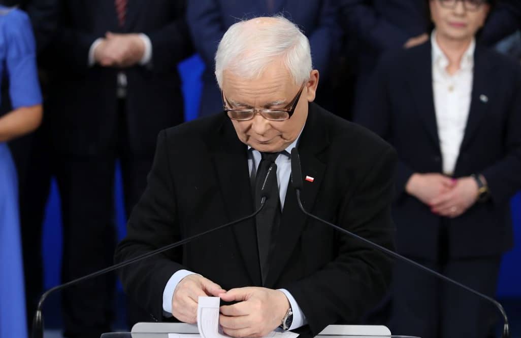 Jarosław Kaczyński w okularach na scenie, za nim stoją politycy PiS