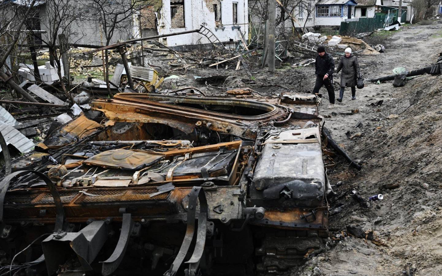 Local residents walk amid debris of a charred Russian tank next to destroyed houses in the village of Zalissya, northeast of Kyiv, on April 19, 2022, during the Russian invasion of Ukraine. (Photo by Genya SAVILOV / AFP)