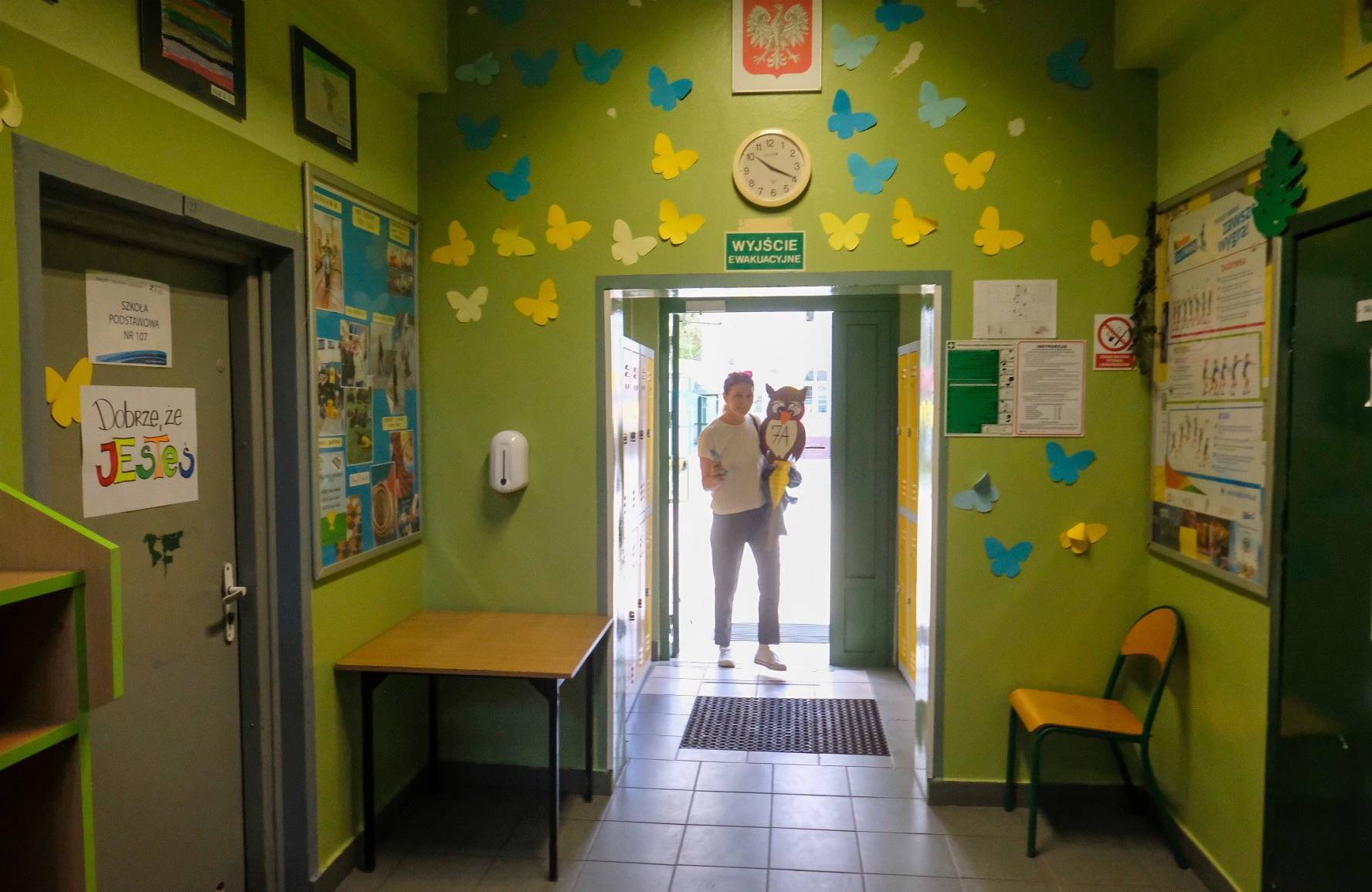 01.09.2022, rozpoczęcie roku szkolnego w szkole podstawowej specjalnej 107 im. Arkadego Fiedlera w Poznaniu. W otwartych drzwiach na końcu zielonego korytarza przystrojonego żółtymi i niebieskimi motylami z papieru, stoi kobieta. W ręku trzyma sowę z papieru, na której widnieje napis "7A"