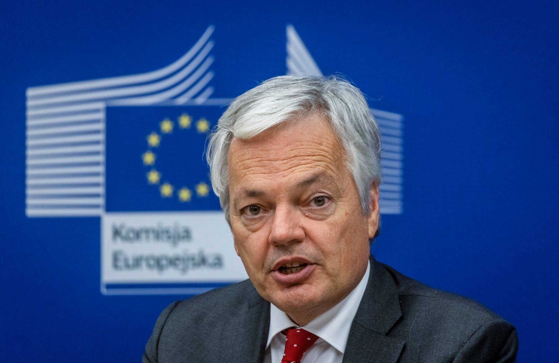 Mężczyzna siwy, Dider Reynders, na tle symbolu Unii Europejskiej