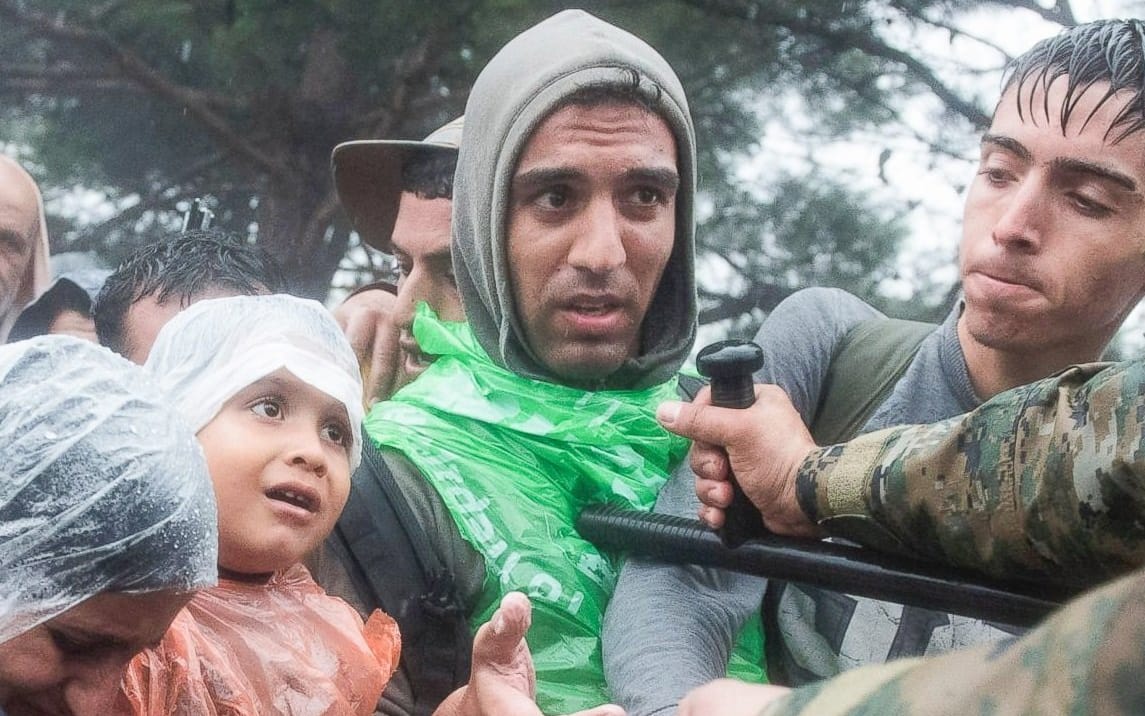 Macedonian border police help refugees and migrants to pass from the northern Greek village of Idomeni to southern Macedonia, Sept. 10, 2015. Thousands of people braved torrential downpours to cross Greece's northern border with Macedonia early Thursday.