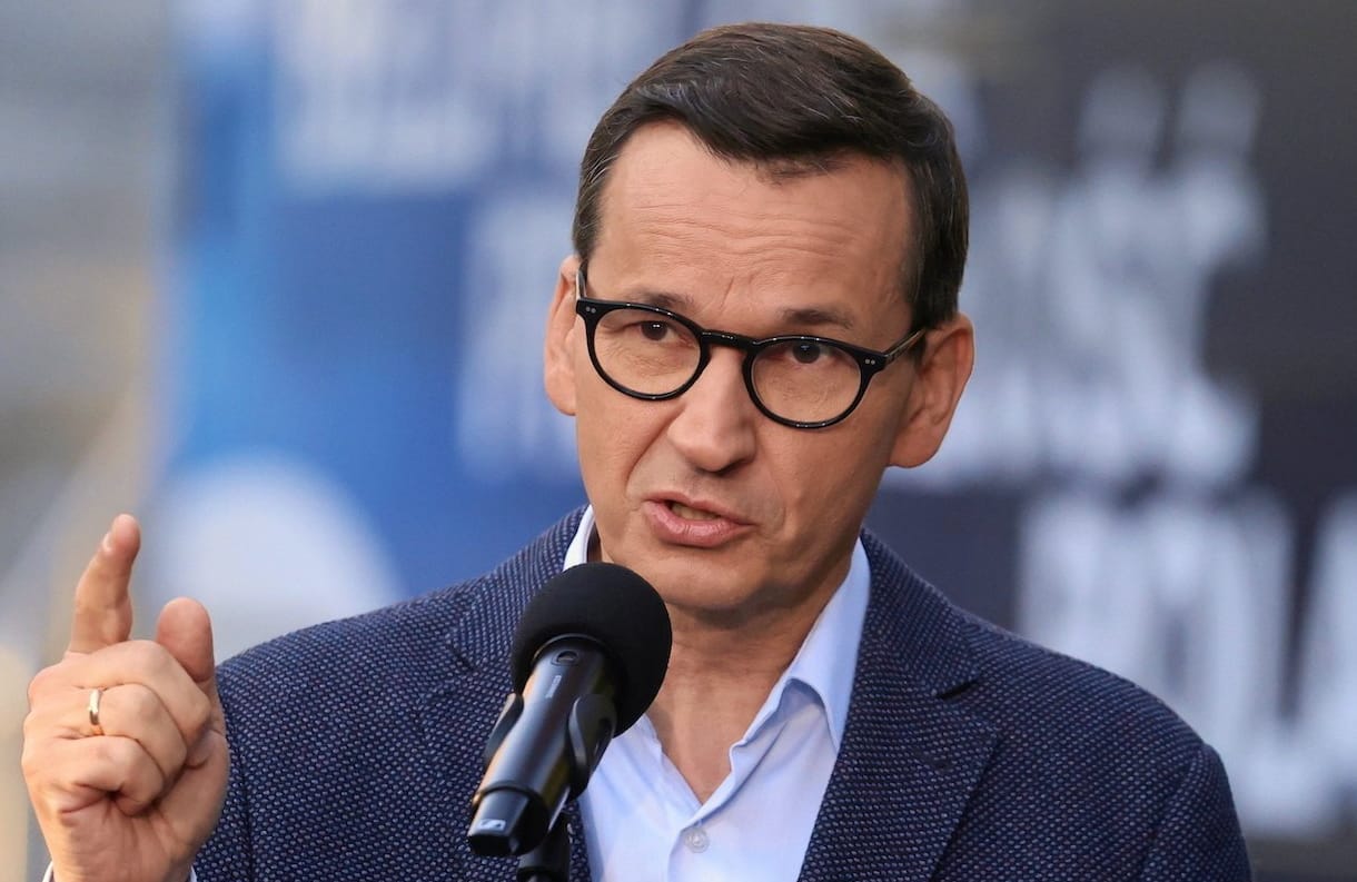 Mateusz Morawiecki przemawia do mikrofonu, unosząc do góry palec wskazujący prawej dłoni.