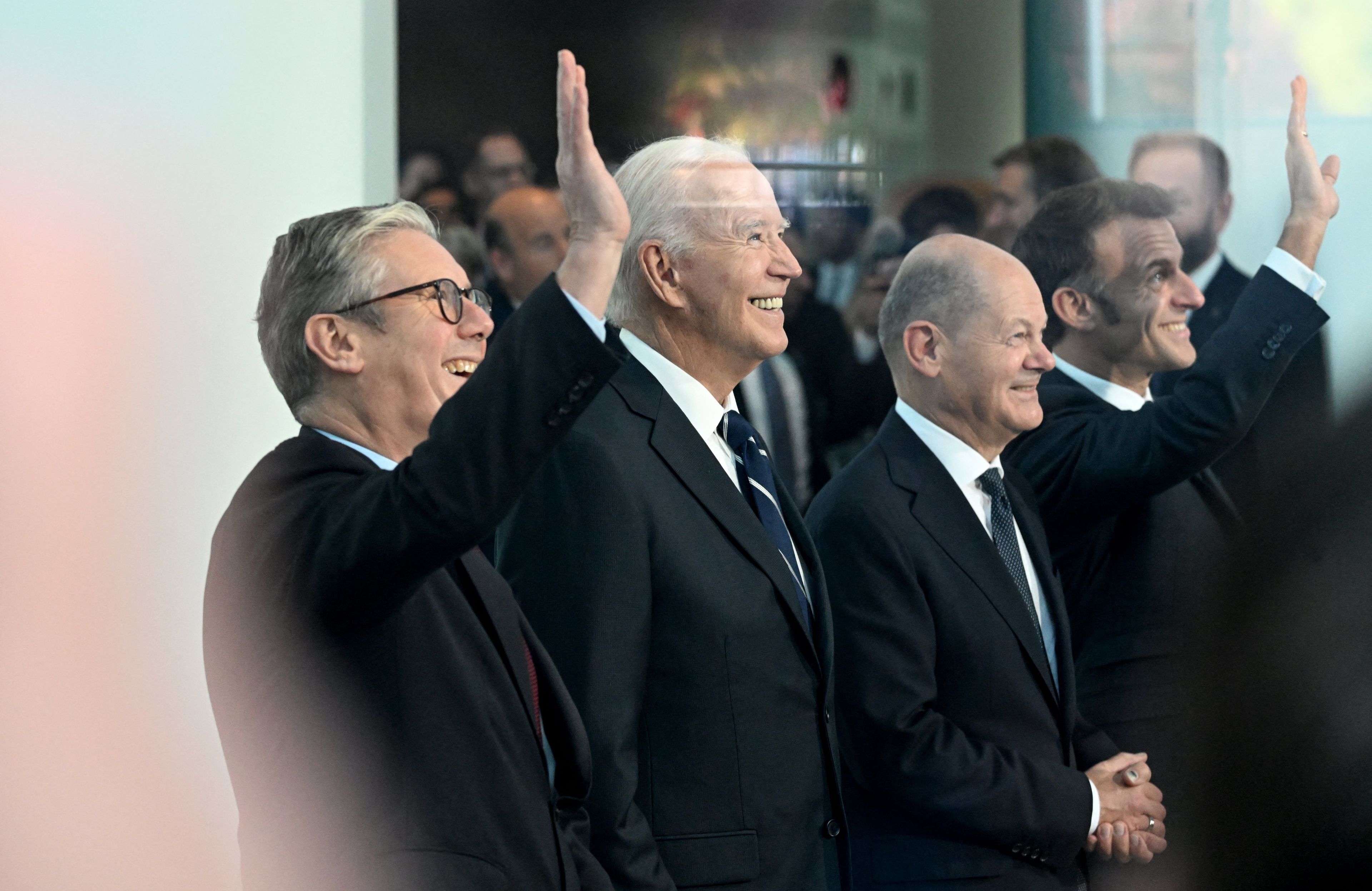Czterech mężczyzn w garniturach uśmiecha się, jeden podnosi rękę