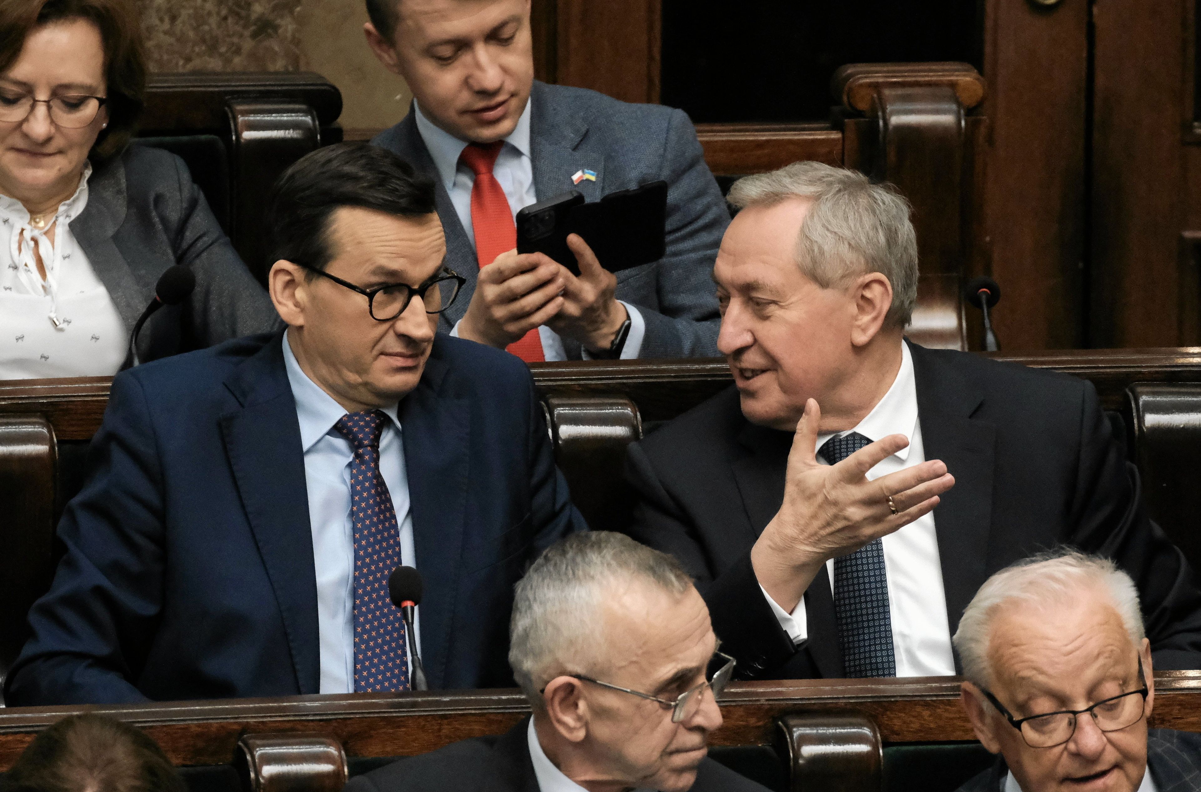 Mężczyźni w garniturach w ławach rządowych w Sejmie. Premier Mateusz Morawiecki robi zdziwioną minę, a minister Henryk Kowalczyk gestykuluje